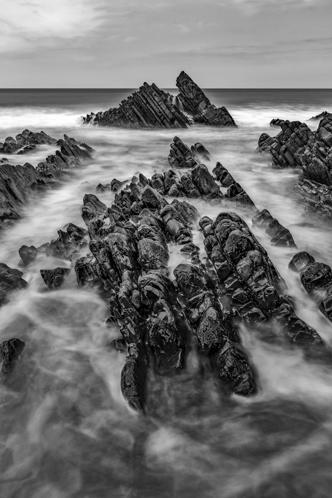 Long exposure of the waves moving over the twisted layers of rocks on Welcombe Beach in the North Devon Area of Natural Beauty.