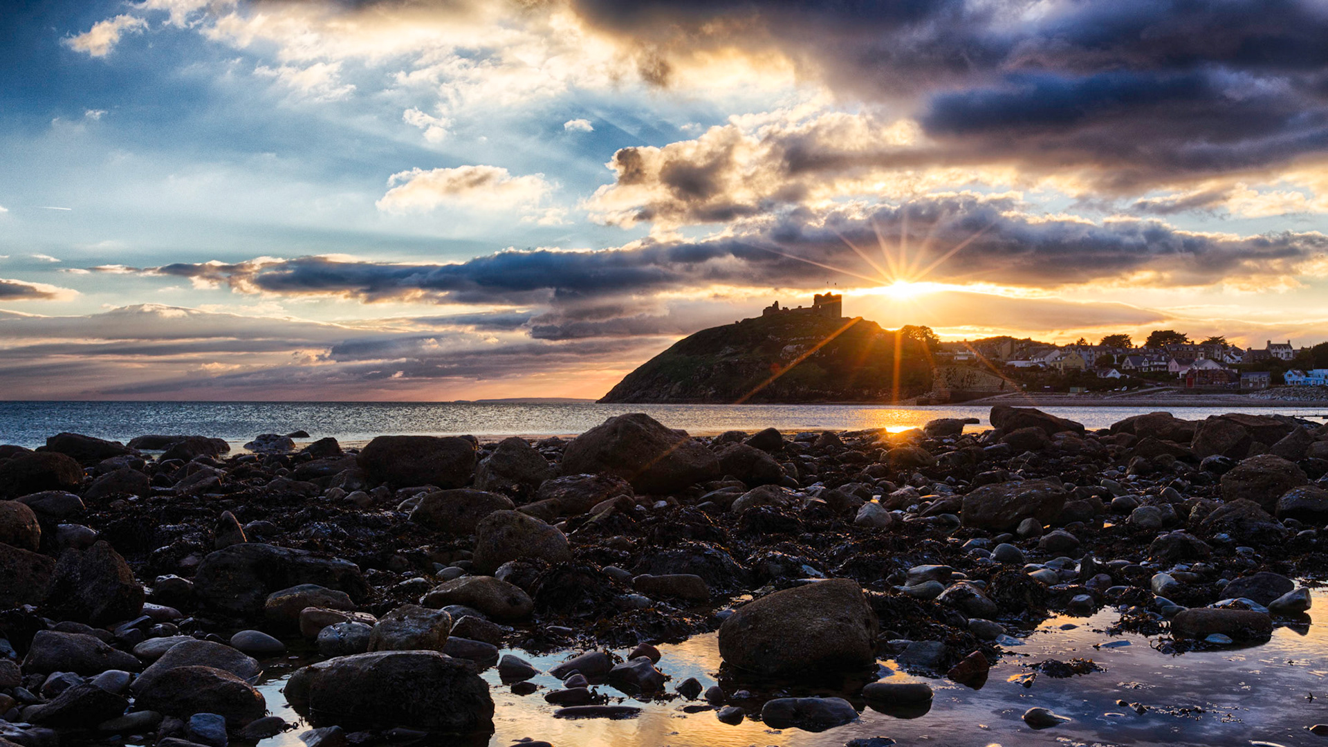 Sunseting behind Criccieth Castle on a Welsh beach. A welsh sea view with the sun setting behind Criccieth castle stood on top the hill overlooking the coast