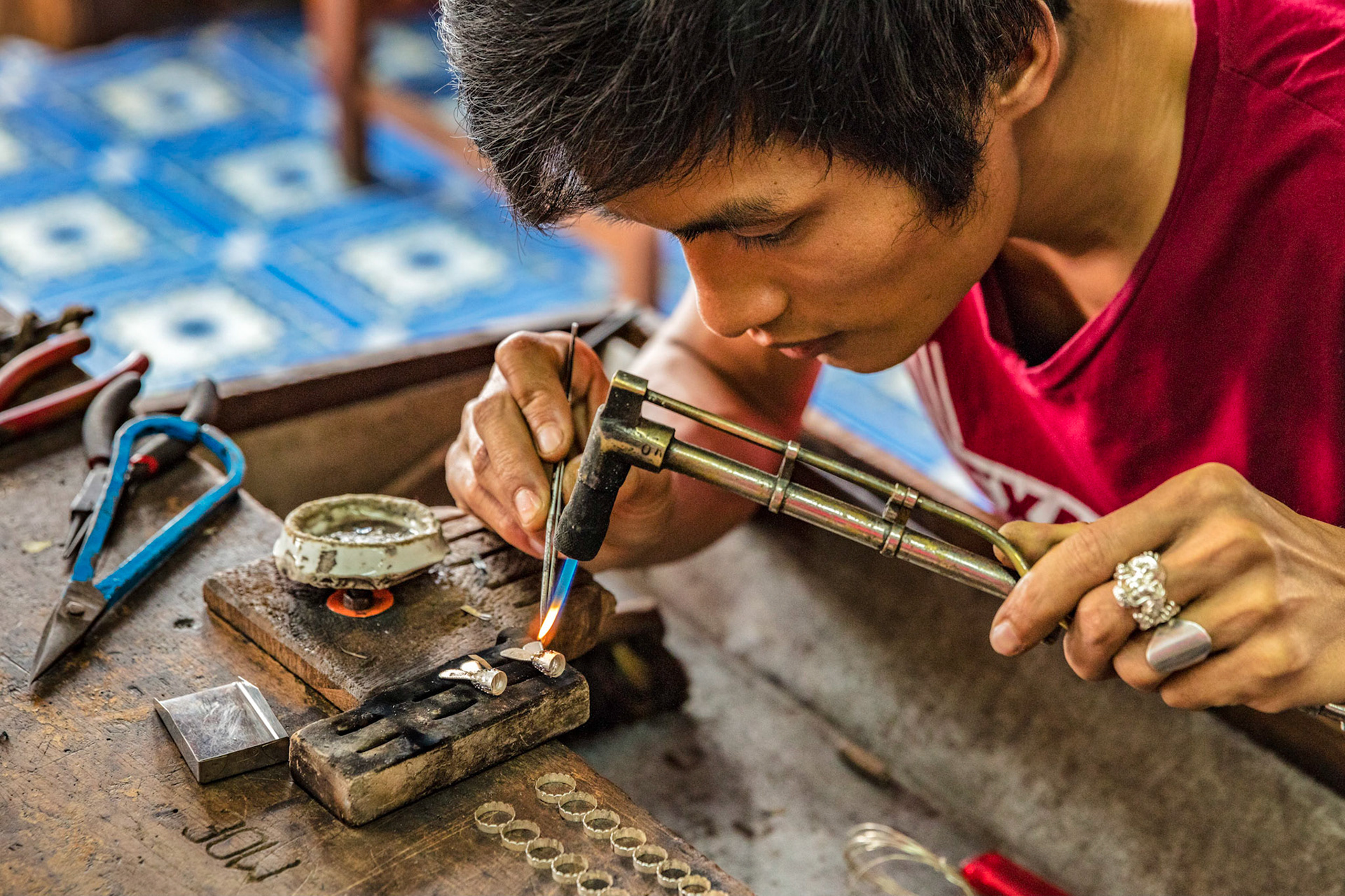 Local Burmese man using a torch to heat up silver shaping it into a piece of jewelry on Inle Lake, Myanmar.