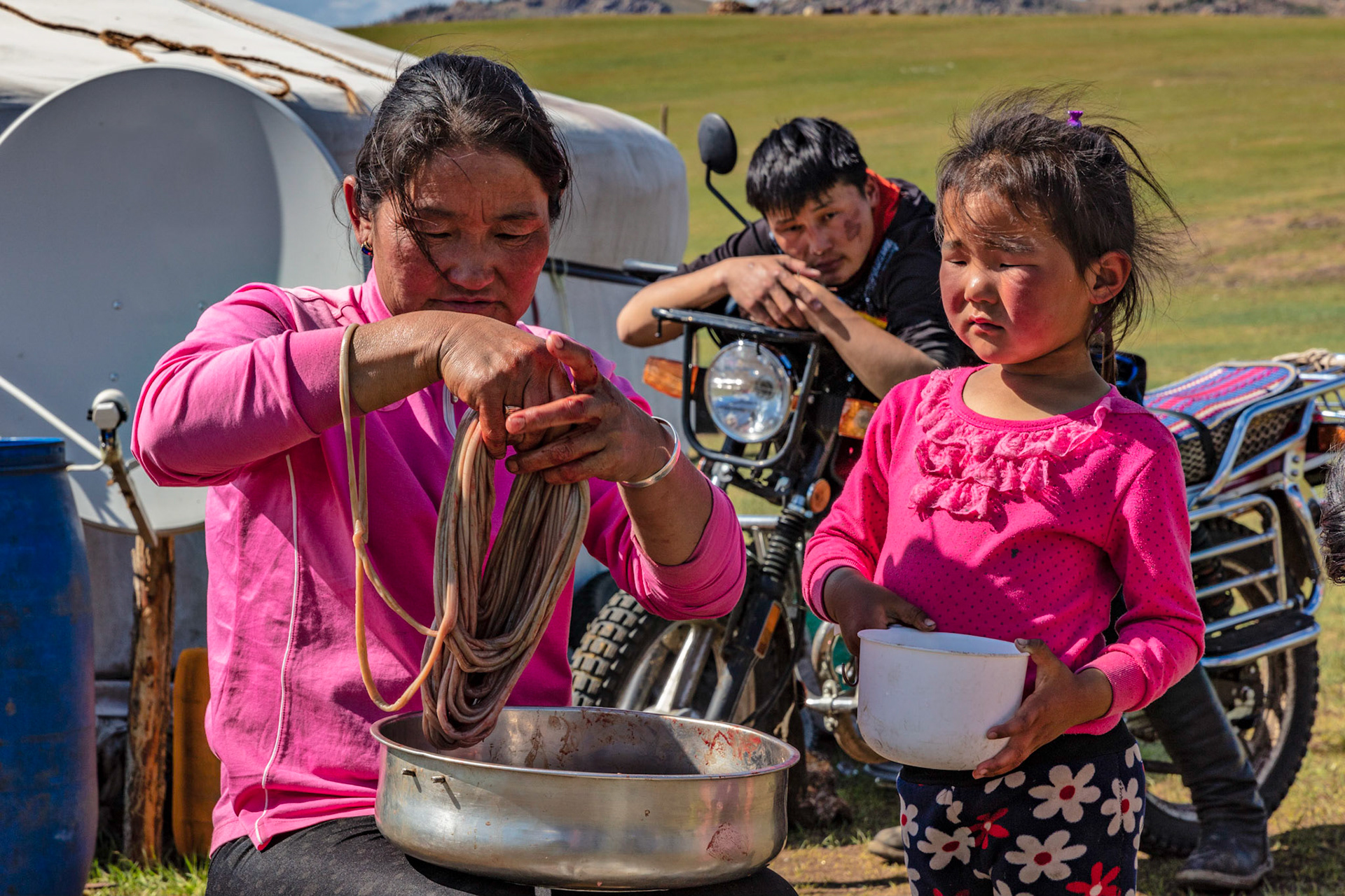 Young Mongolian girl helping out as the elder woman arranges the intestines and the eldest son looks on.