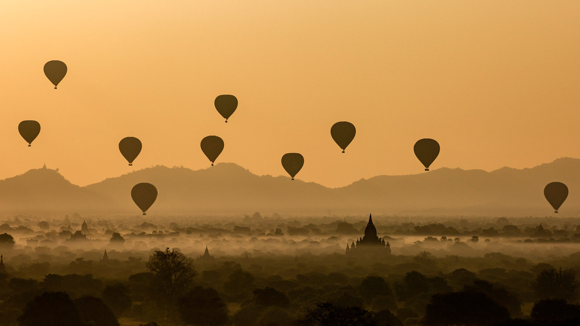 Hot air balloons floating over the abandoned stupas illuminated in the golden light of the rising sun of Bagan, Myanmar.
