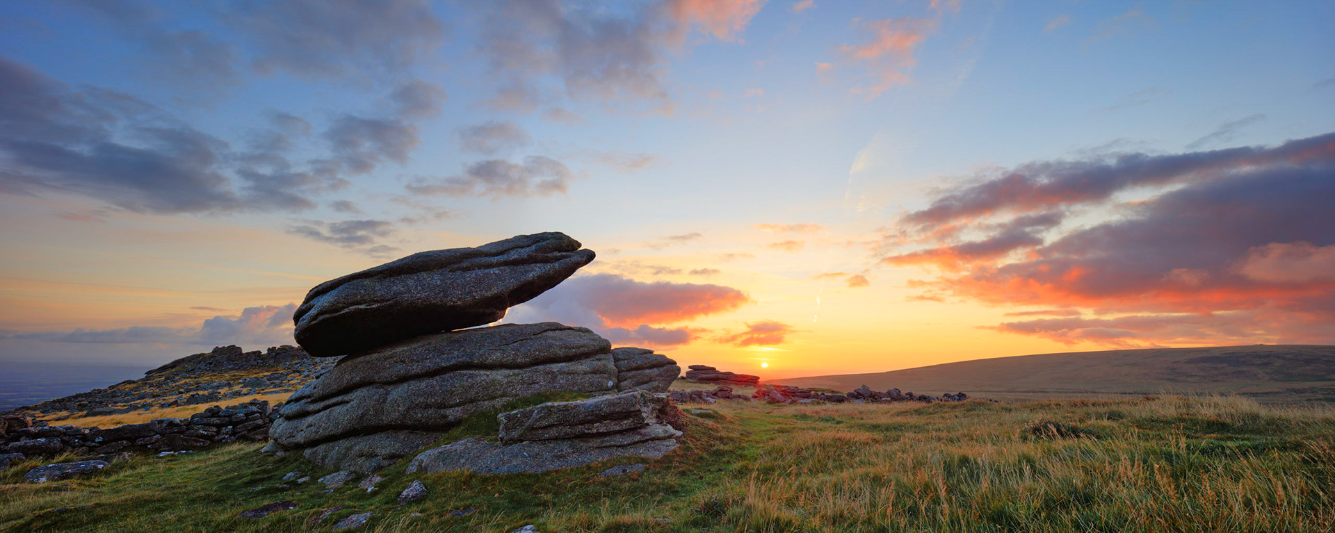 Early morning near Belstone Tor in Dartmoor National Park with the sun rising behind a logan stone.