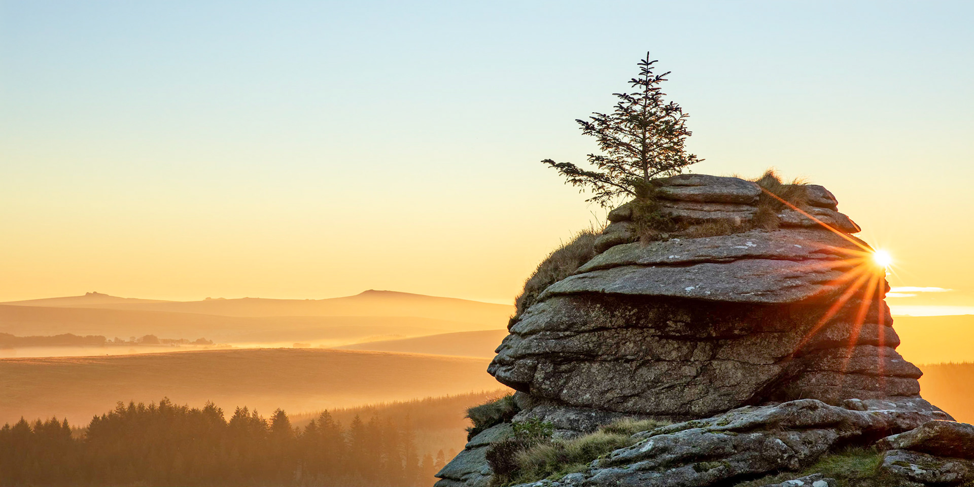 Golden hour in Dartmoor National Park with the sun illuminating the mist rising from the rolling moorland hills taken from Bellever Tor.
