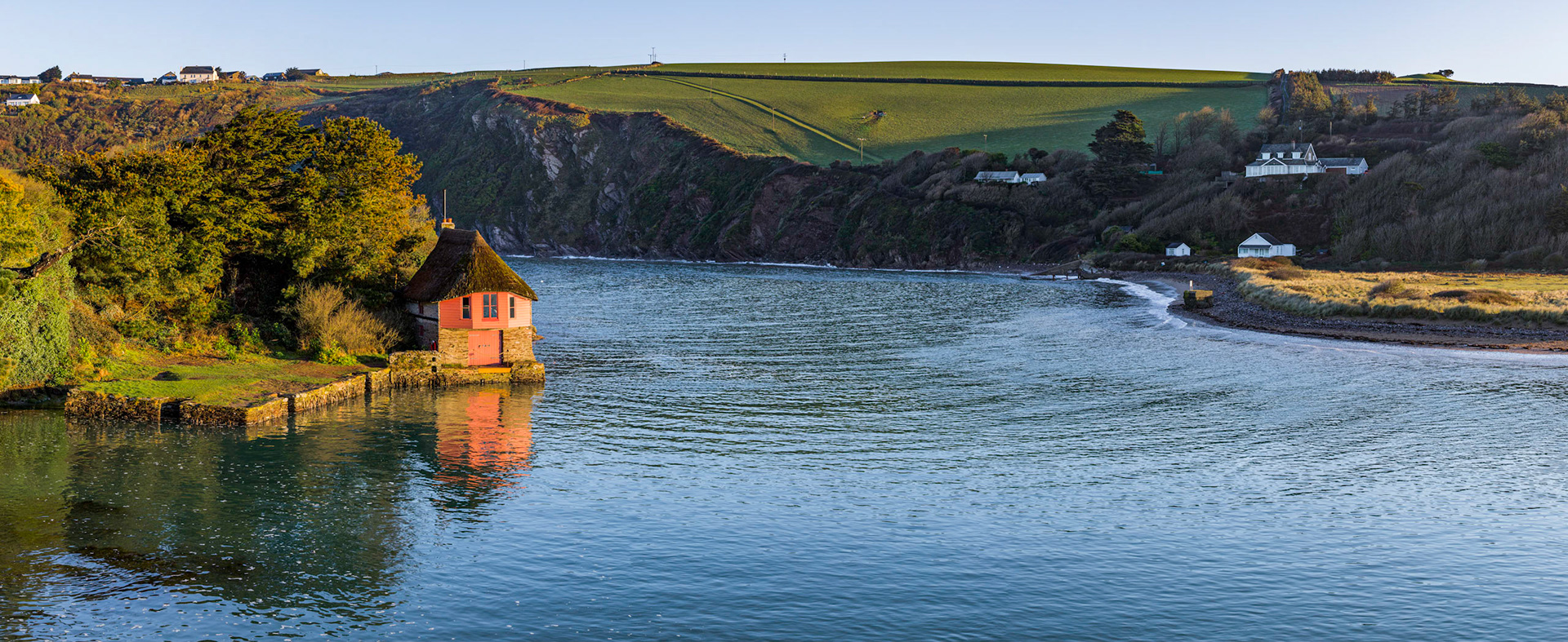 Shortly after dawn as the sun illuminates the old quaint boathouse and the surrounding countryside. The boathouse sits along side the river Avon near the village of Bantham along England's southern coast.