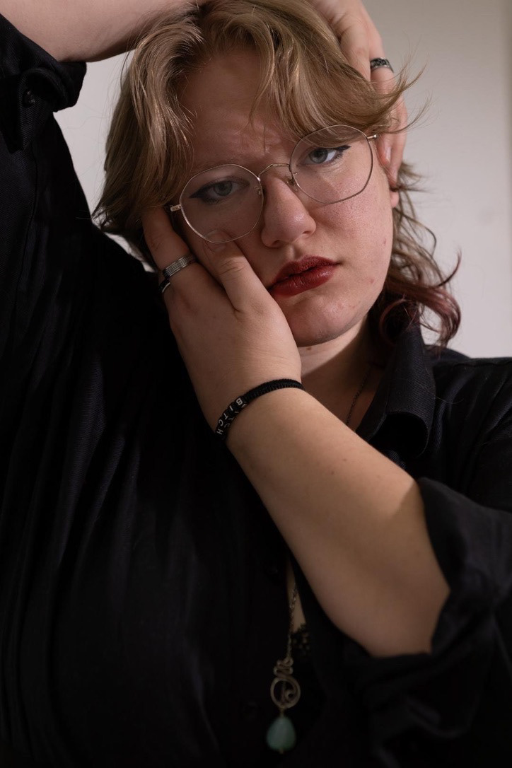 image of a person with blonde hair, their head is tilted to the side and their hands are cupping their face anymetrically