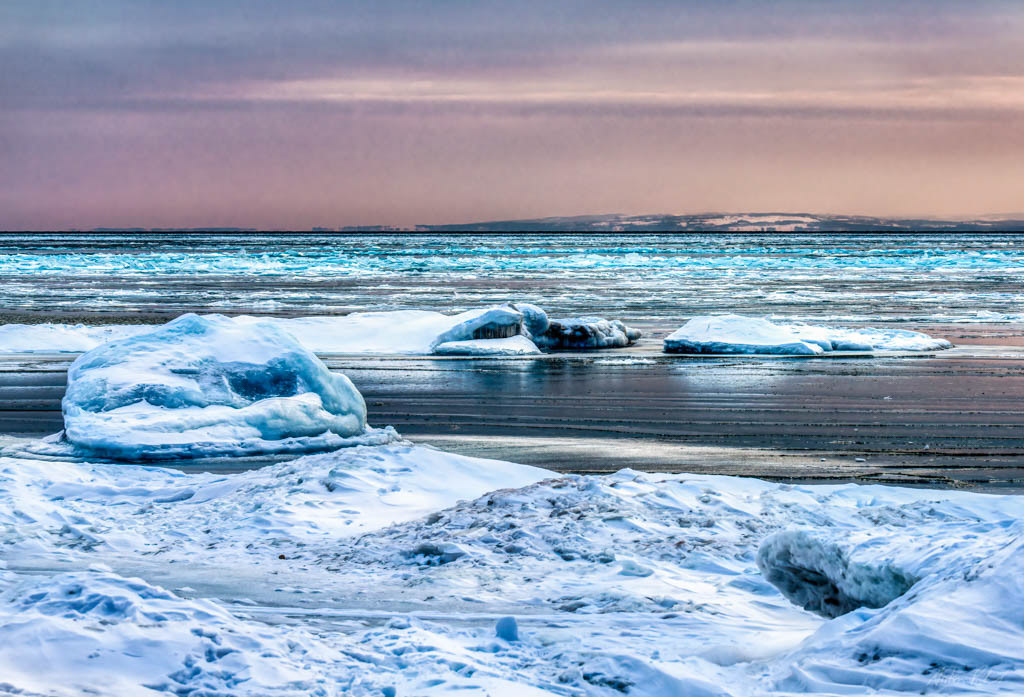 winter photo of ice on a lake - hills in the distance