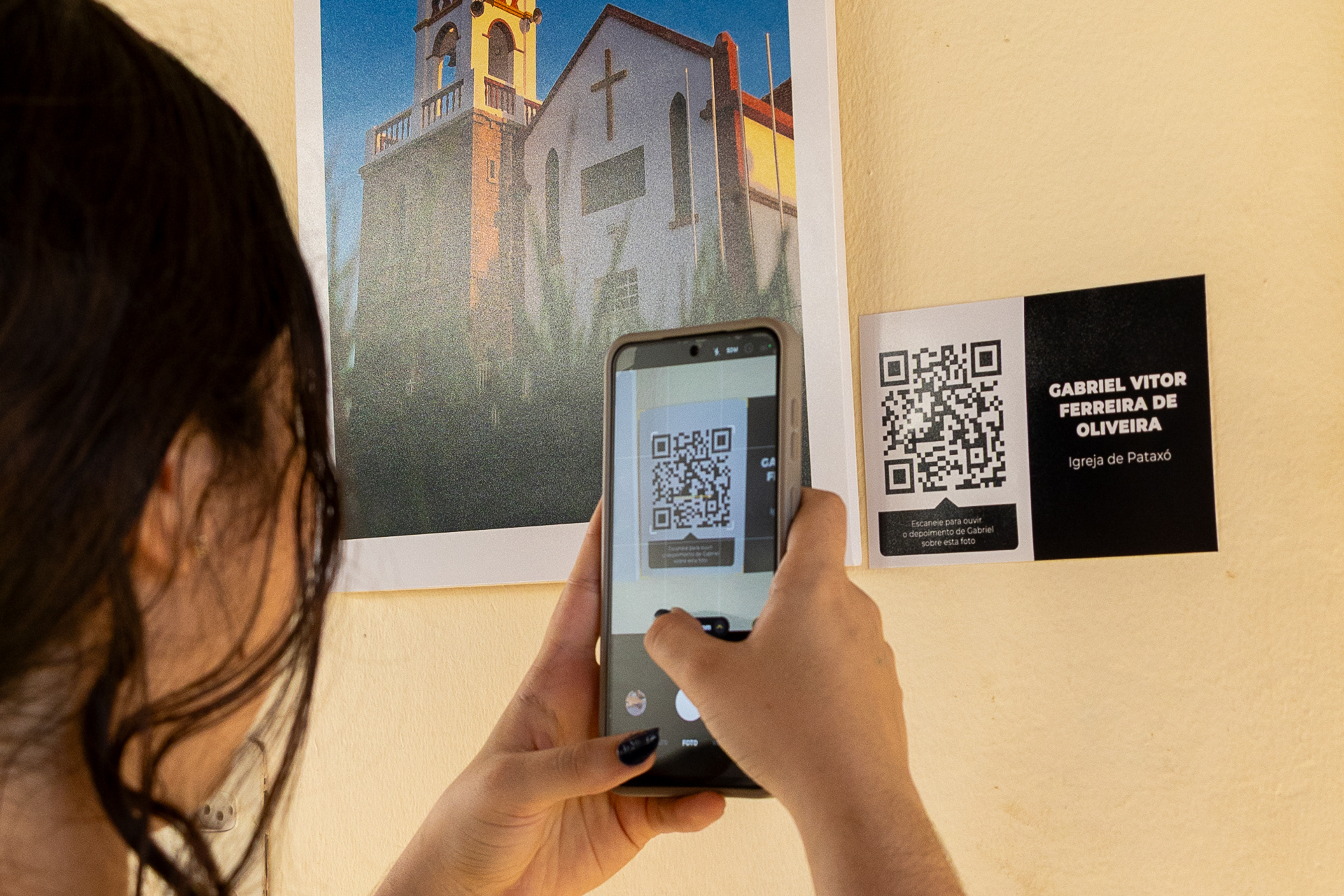 Visitante da exposição escaneia QR code que acompanha a foto do aluno Gabriel