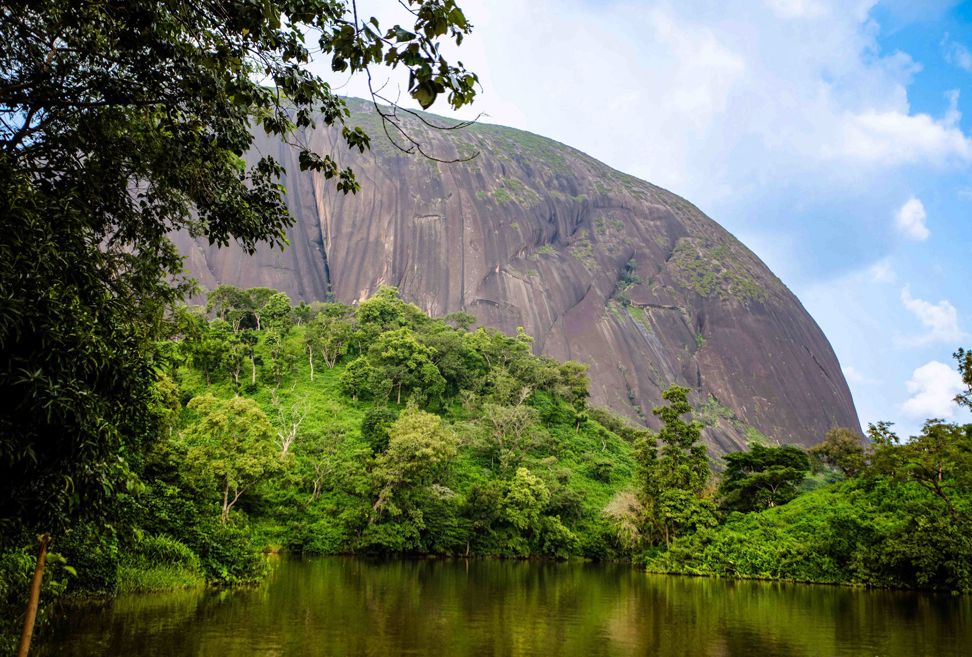 A mountain rises behind dense tropical vegetation, creating a quiet contrast between nature’s growth and decay. The landscape reflects the passage of time, endurance and the changing environment.