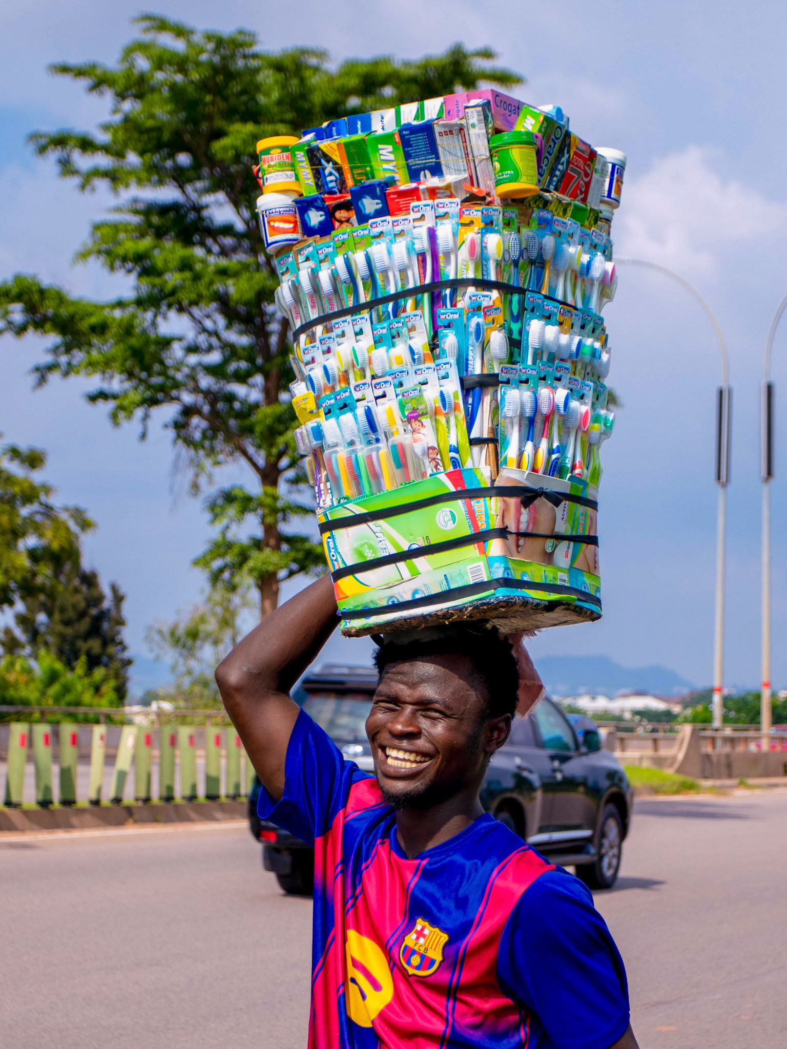 A vendor balances an expansive display of personal-care products while moving through the streets, capturing the energy, dignity and resilience of informal commerce.