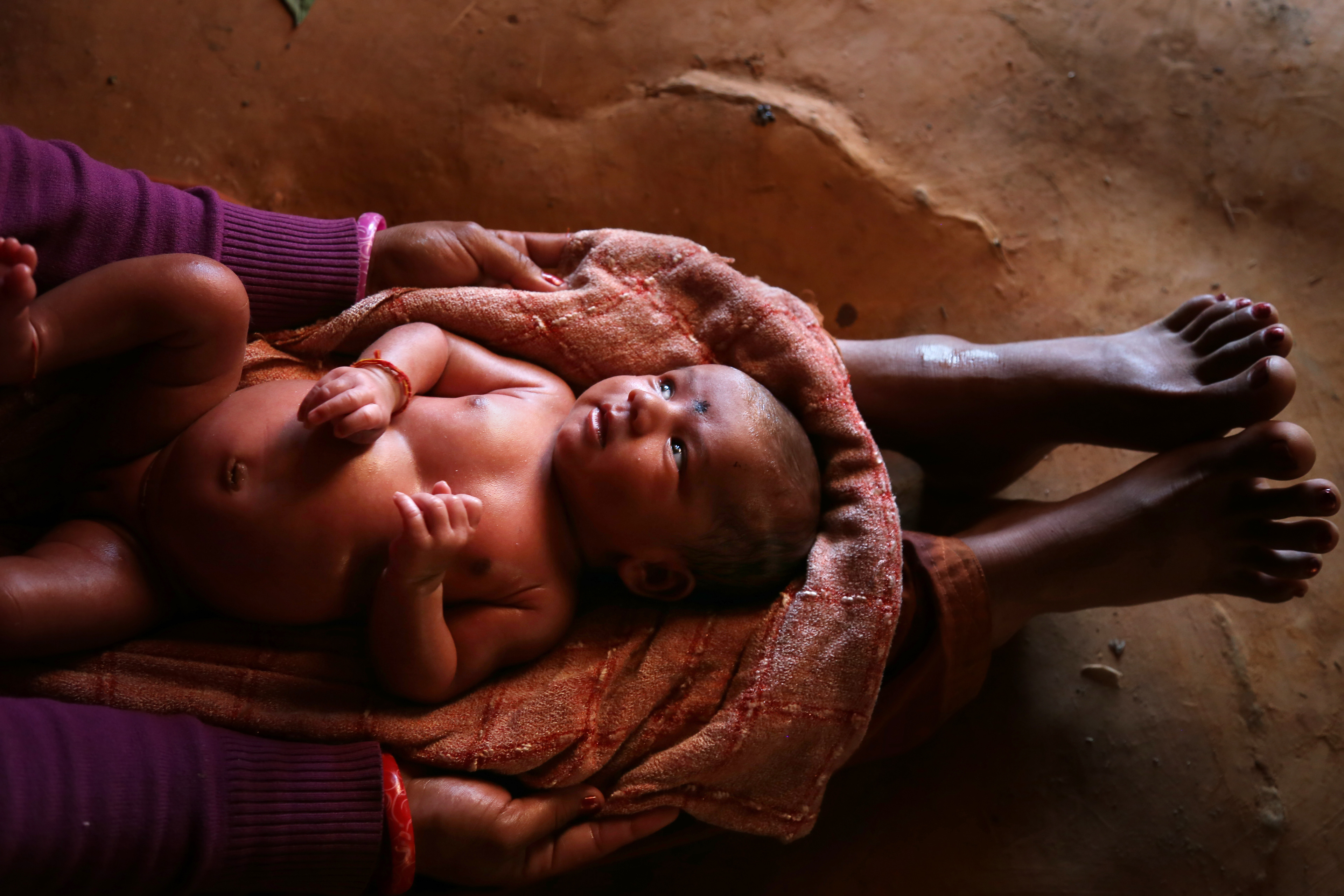 A young mother cradles her baby shortly after the baby received it's first vaccines. Nepal, 2015