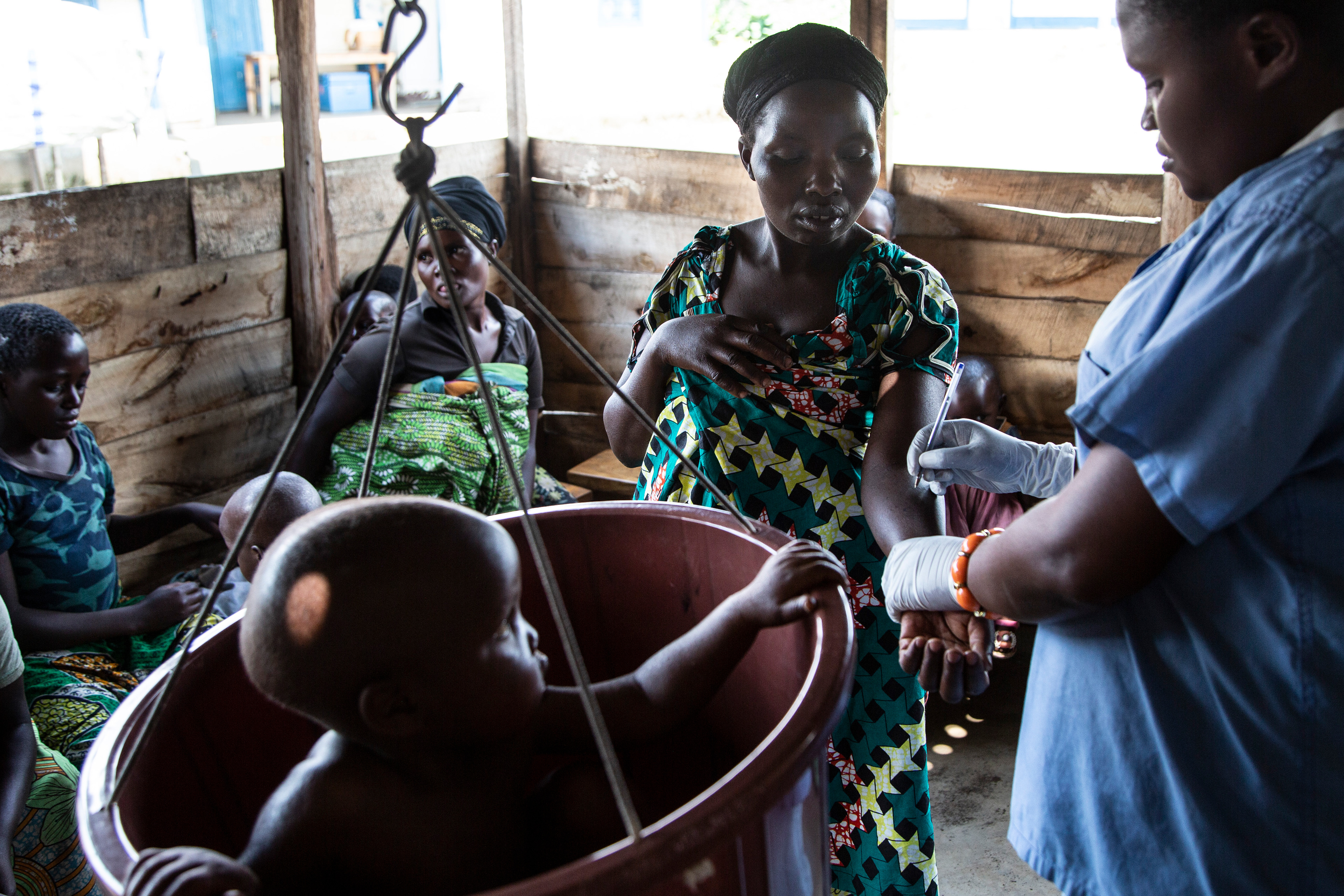 Nurse Ange Amani writes on the arm of the mother of a malnourished child, as the woman does not have a chart or other way of recording the statistics for her child, sitting in the weight scale. 