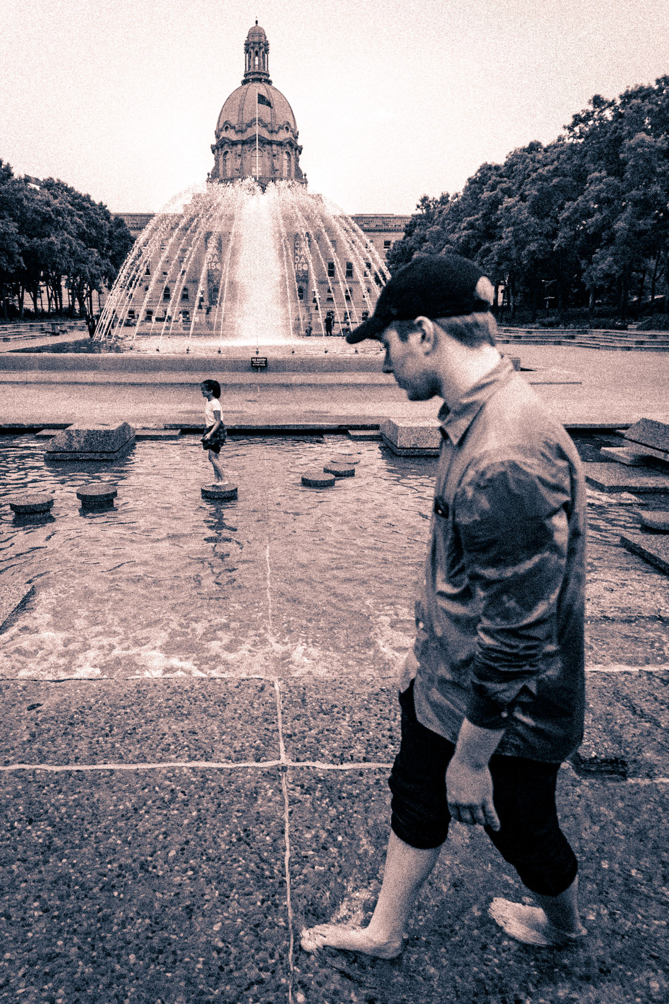 A street photo shot at Edmonton Parliment as folks stroll through the pool