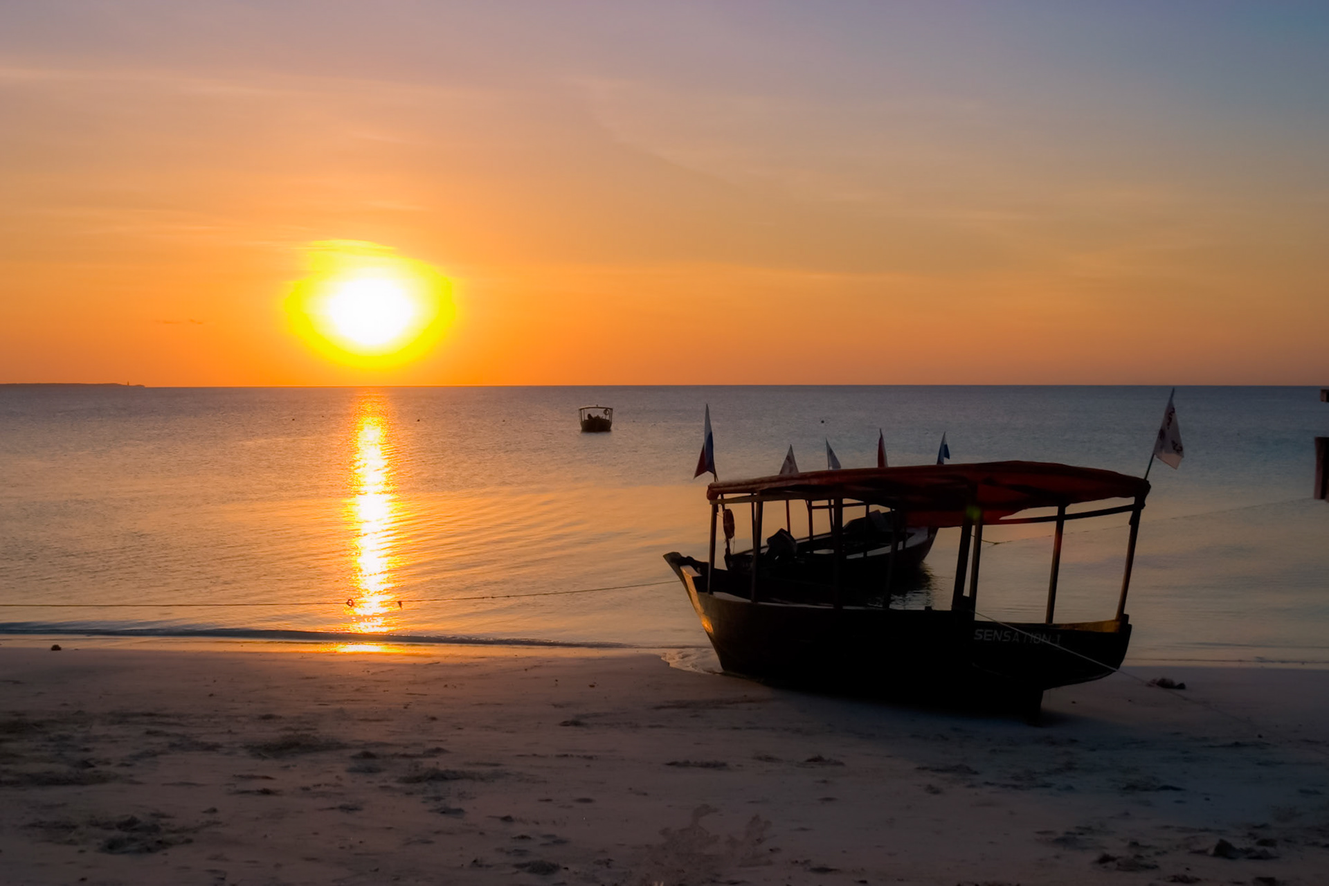 A boat sits on a Zanzibar beach here as both the tide and sun leave.
