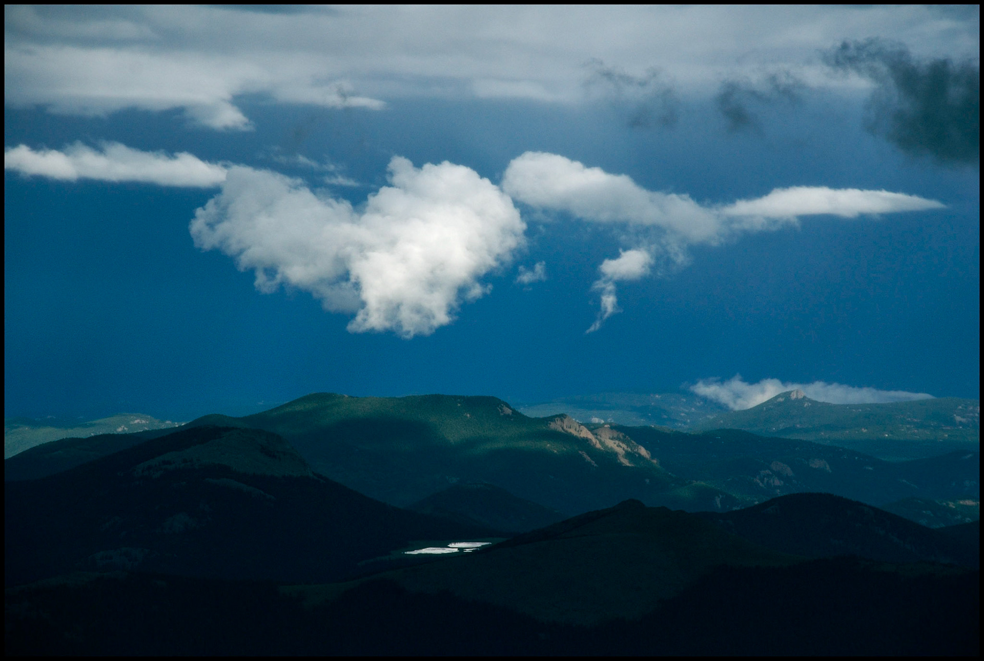 Colorado Rocky Mountain scenic of low hanging clouds against a dark sky above a highlighted mountain top and lake as viewed from Mount Evans Highway, Colorado USA, the highest paved road in the country.