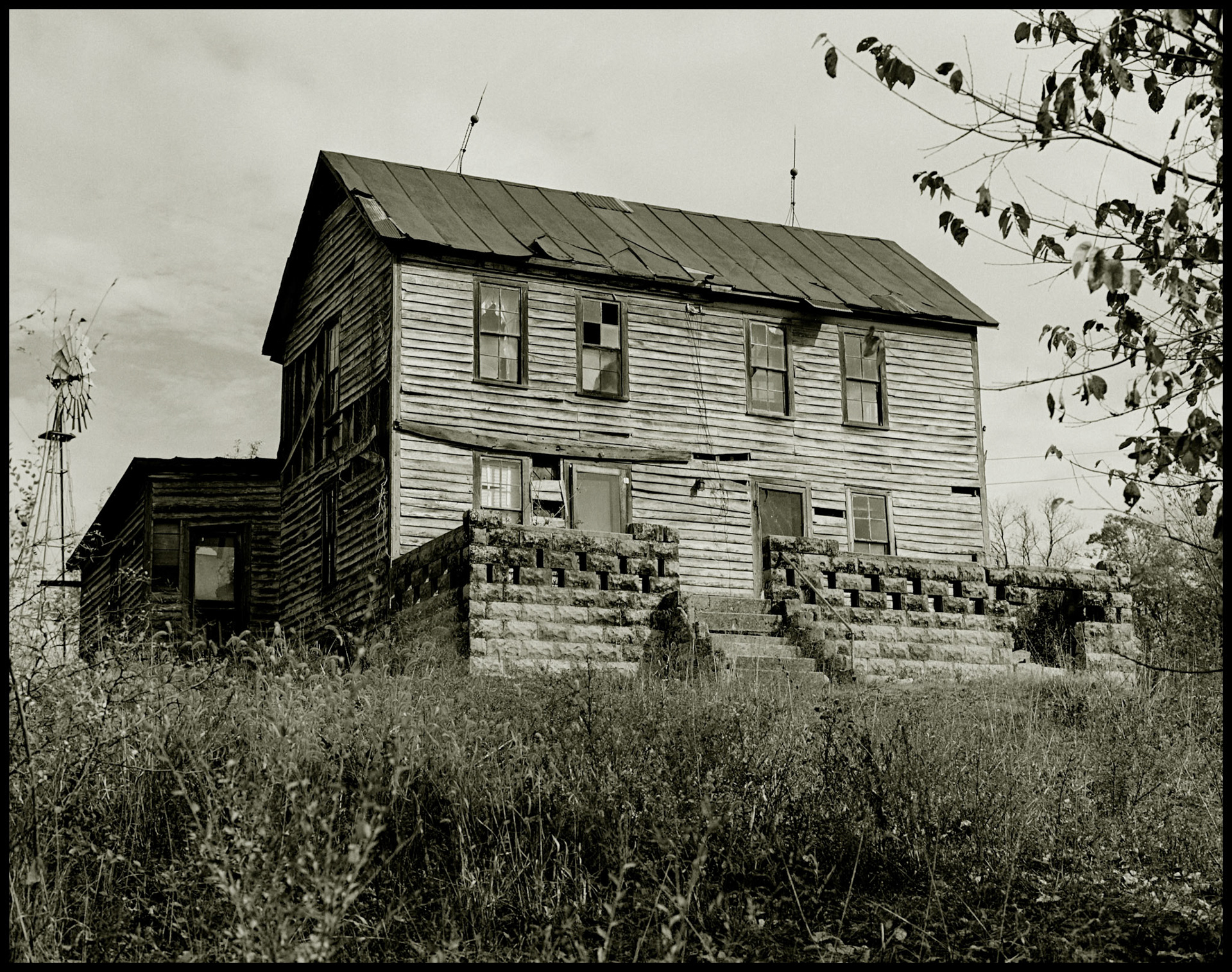A sepia toned black and white vintage image of an abandoned house on a hilltop with a windmill out back in rural Northern Misouri. Yarrow, Missouri, USA, 1978.