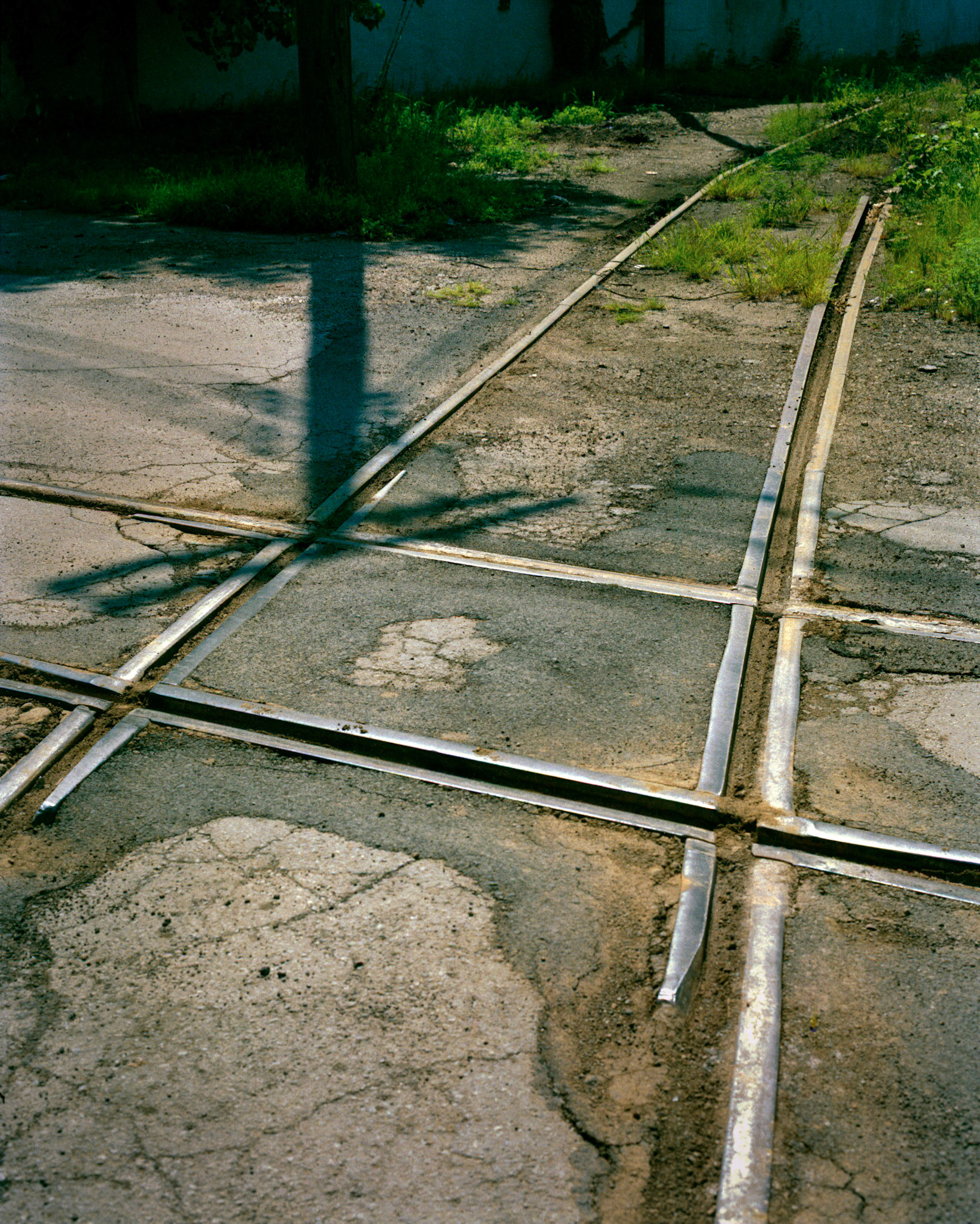 A conceptual cityscape detail of the intersection of two embedded railroad tracks through an industrial area with the intersecting shadow of a power pole and  lines. West Bottoms, Kansas City, Missouri, 1990