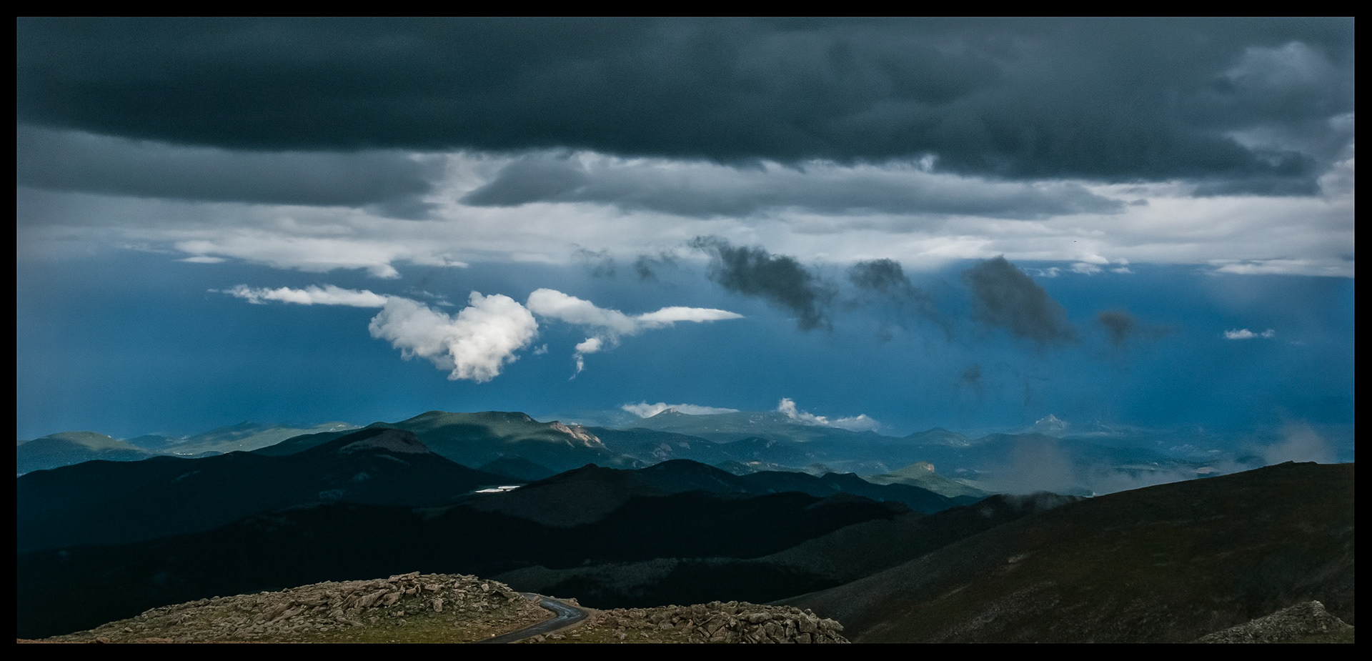 Colorado Rocky Mountain scenic view of low hanging clouds against a dark sky above a highlighted mountain top and lake as viewed from Mount Blue Sky Scenic Byway, near Idaho Springs, Colorado, the highest paved road in the country. 2007.