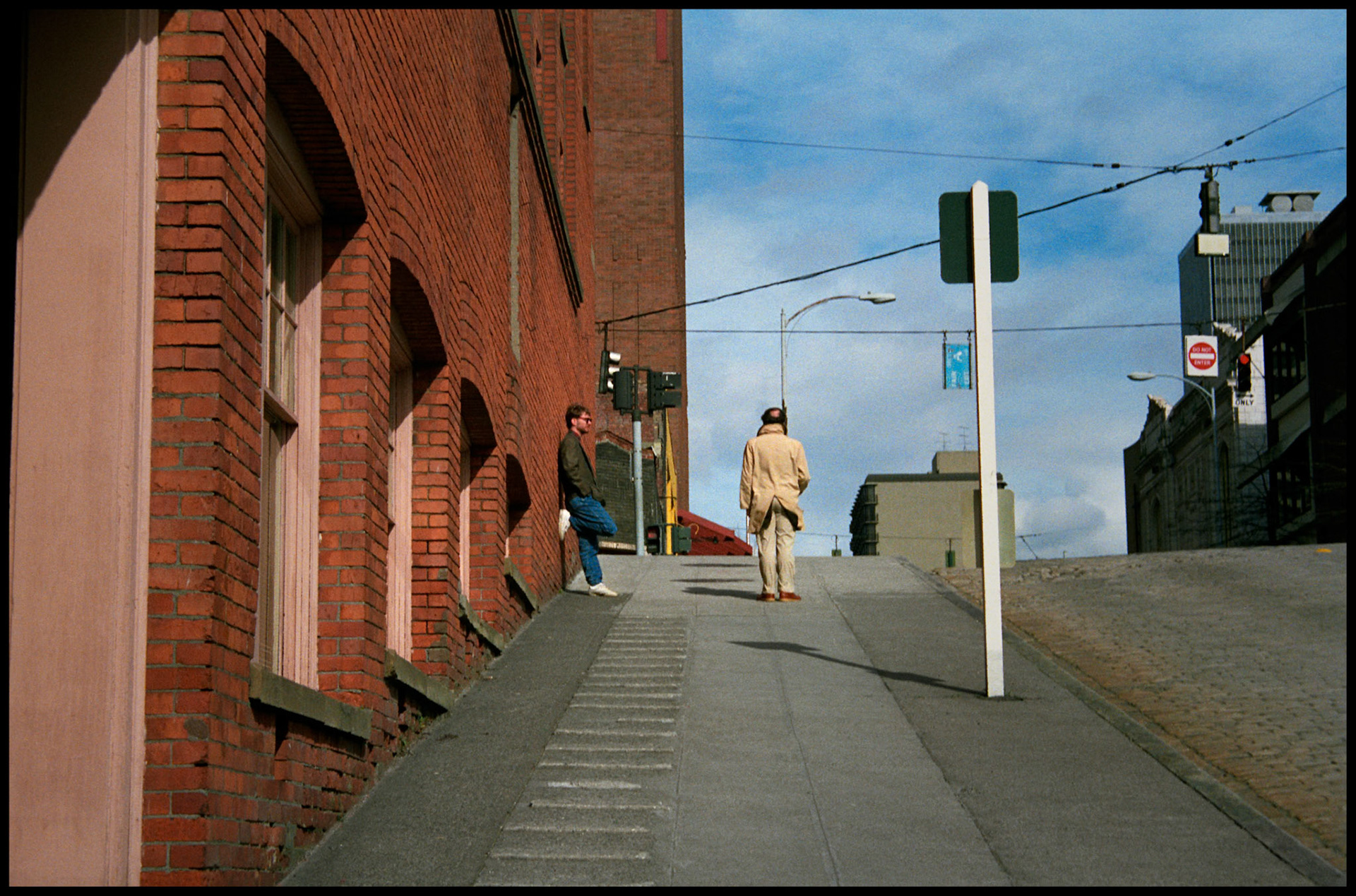 A vintage urban street scene looking up the steep incline toward two men at the corner of First Ave. and Lenora Street in Seattle, Washington USA 1987