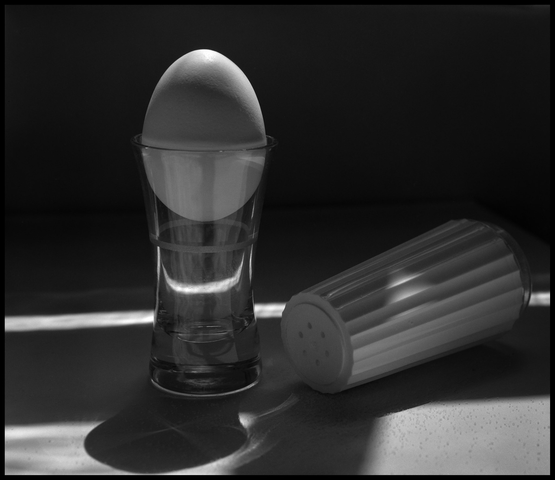 A minimal abstract still life  composition of an egg in an egg cup and salt shaker backlit by the morning sun. Kirksville, Missouri 1984