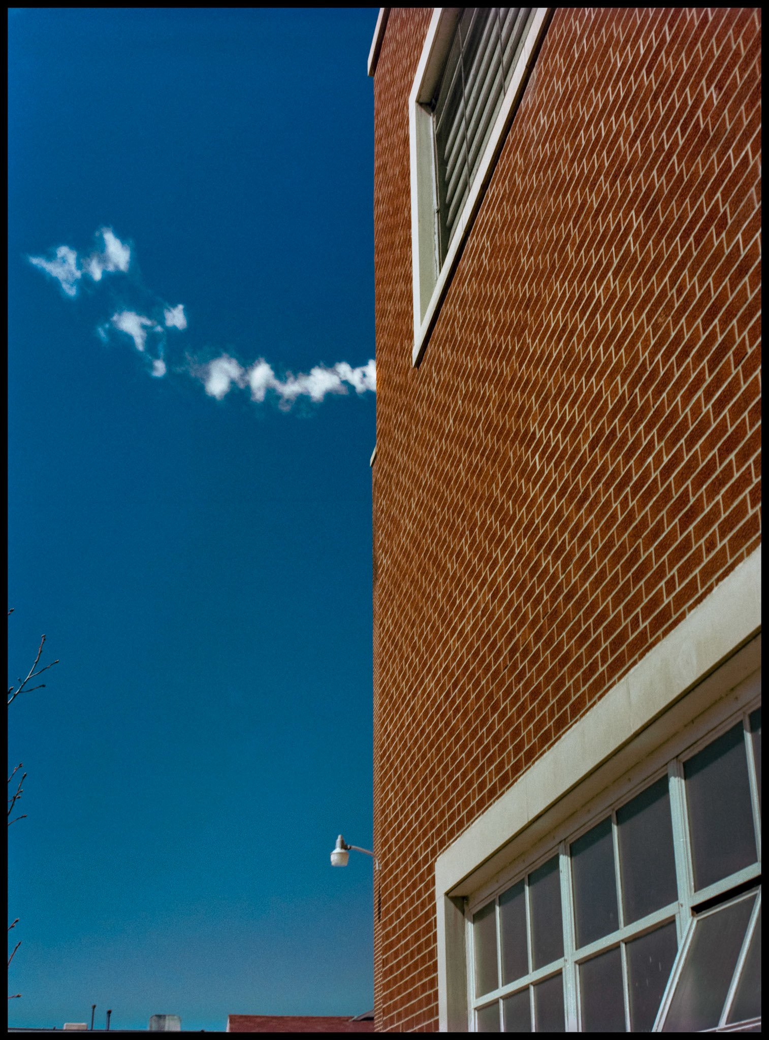 A minimal abstract detail of a brick wall with white windows eminating puffs of steam against a deep blue sky on the Northeast Missouri State University (Since renamed Truman State University) Physical Plant building. Kirksville, Missouri 1981