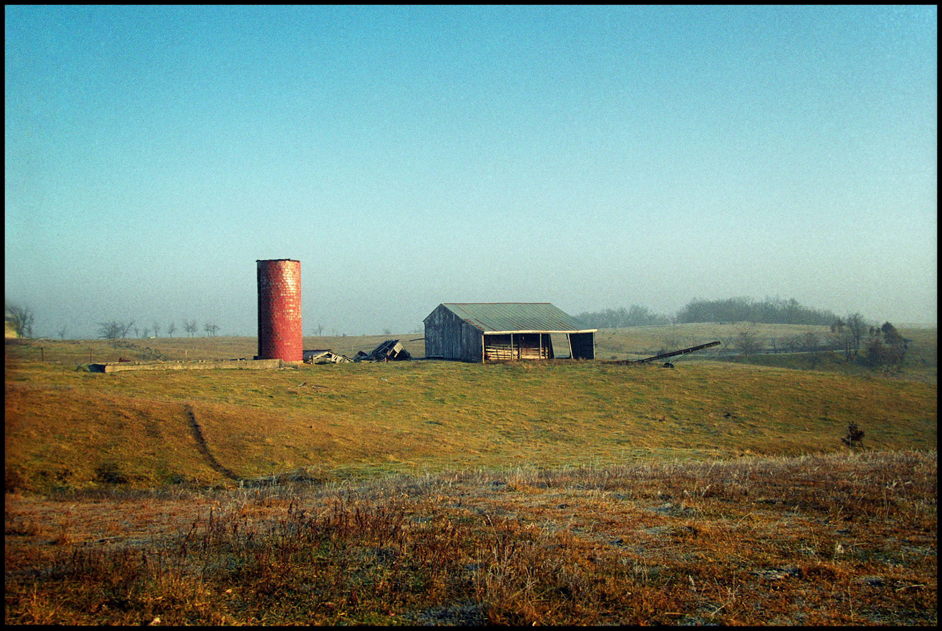 A barn and red brick grain silo on a hillside on a misty morning. Near Pure Air, Missouri, 1994.