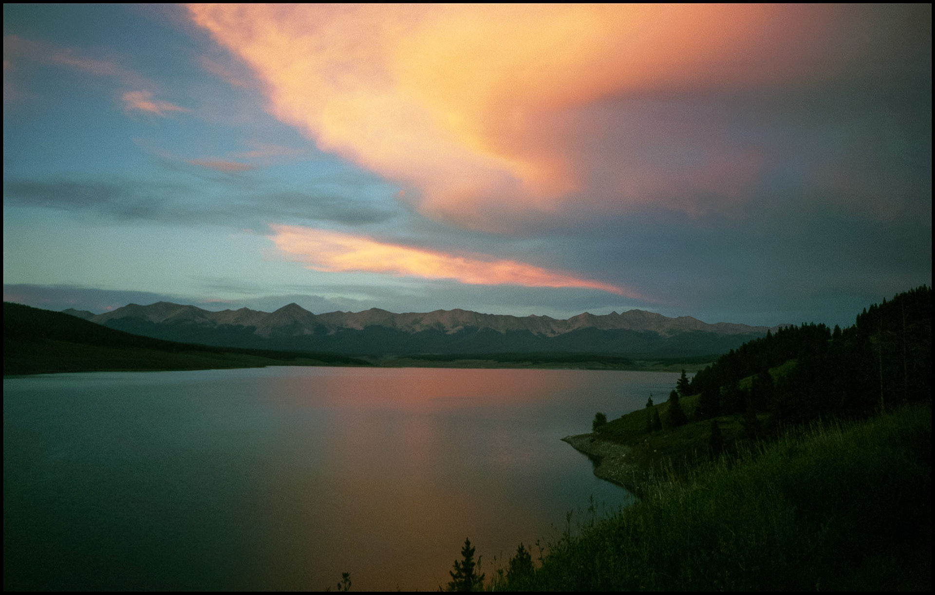 Sweeping colorful clouds and mountain range lit by the sunset with Taylor Park's Taylor Resevoir Colorado in the foreground. The mountains in the distance are part of the Collegiate Peaks in the Sawatch Range near Cottonwood Pass, near Tincup Colorado 1998