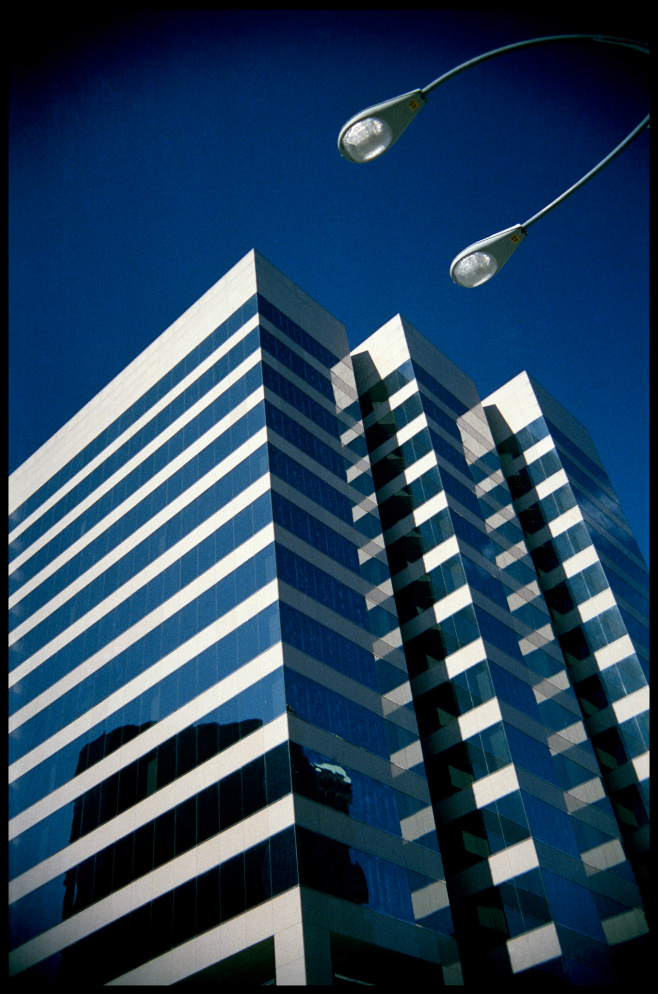A minimal abstract view of the Peabody Building in downtown St. Louis with mirrored windows and streetlight looming overhead. Part of An Afternoon in St. Louis series, St. Louis, Missouri, 1988.