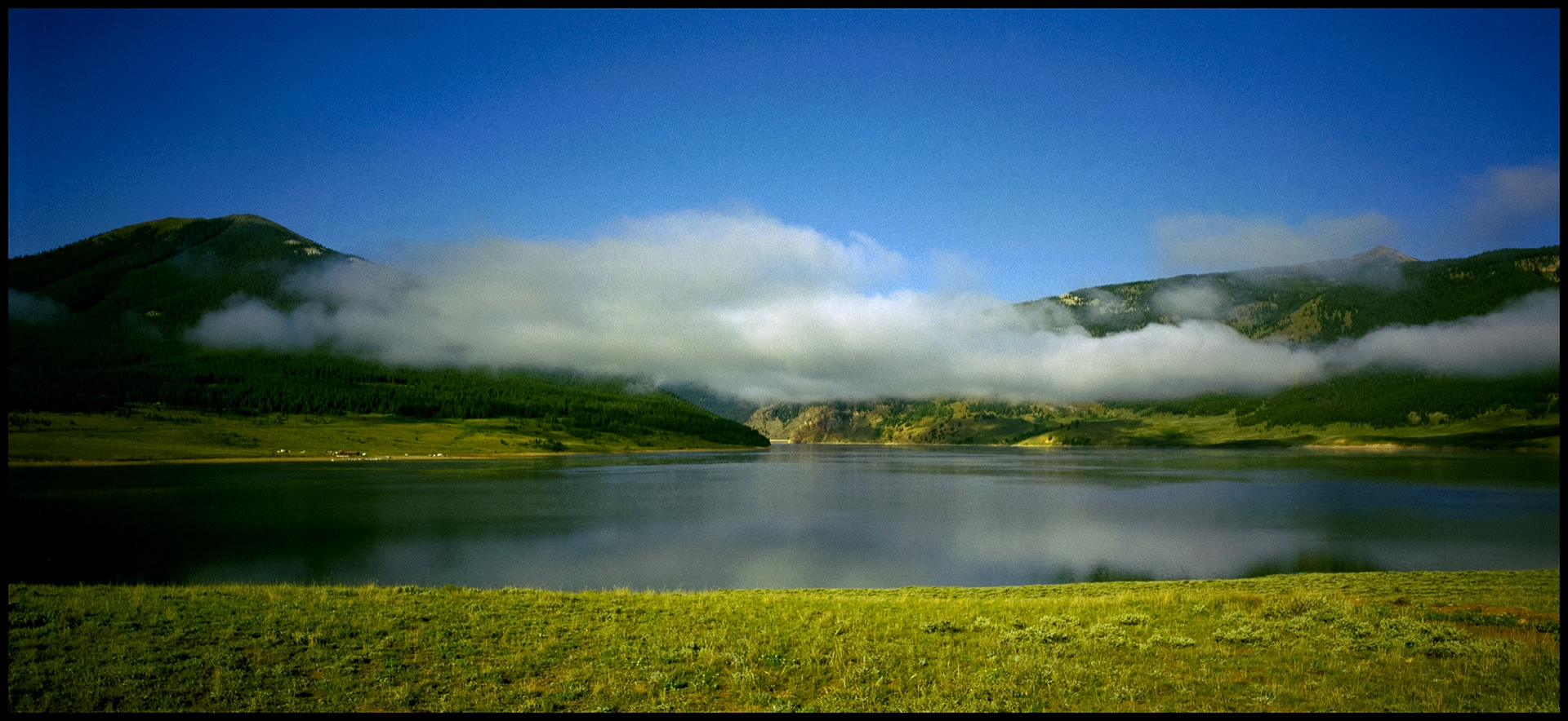 A panoramic landscape showing a morning low hanging cloud above Taylor Reservoir with the surounding mountains and Taylor dam in the background. Near Tin Cup, Colorado. 1998.