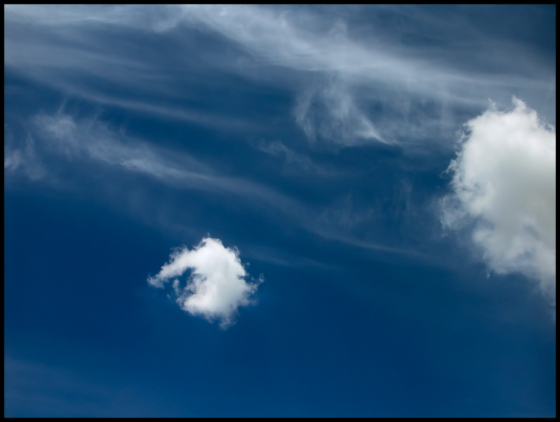Whispy cirrus clouds shooting out diagonally behind stratus clouds contrasted by a dark blue sky in Centralia Missouri