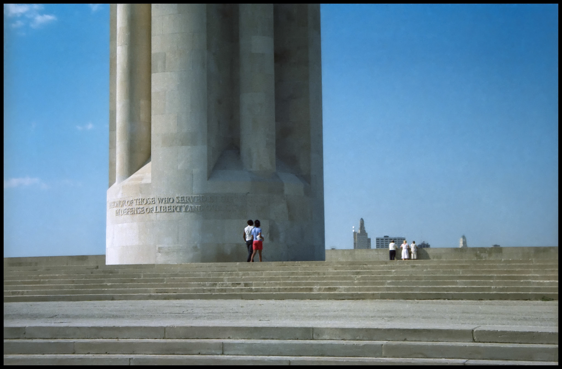 A vintage detail image of the base of the Liberty Memorial Tower and steps at Liberty Memorial Park showing visitors strolling by and viewing the Kansas City skyline in the background. This was renamed as The National World War 1 Museum and Memorial in 2004, Kansas City, Missouri 1983.