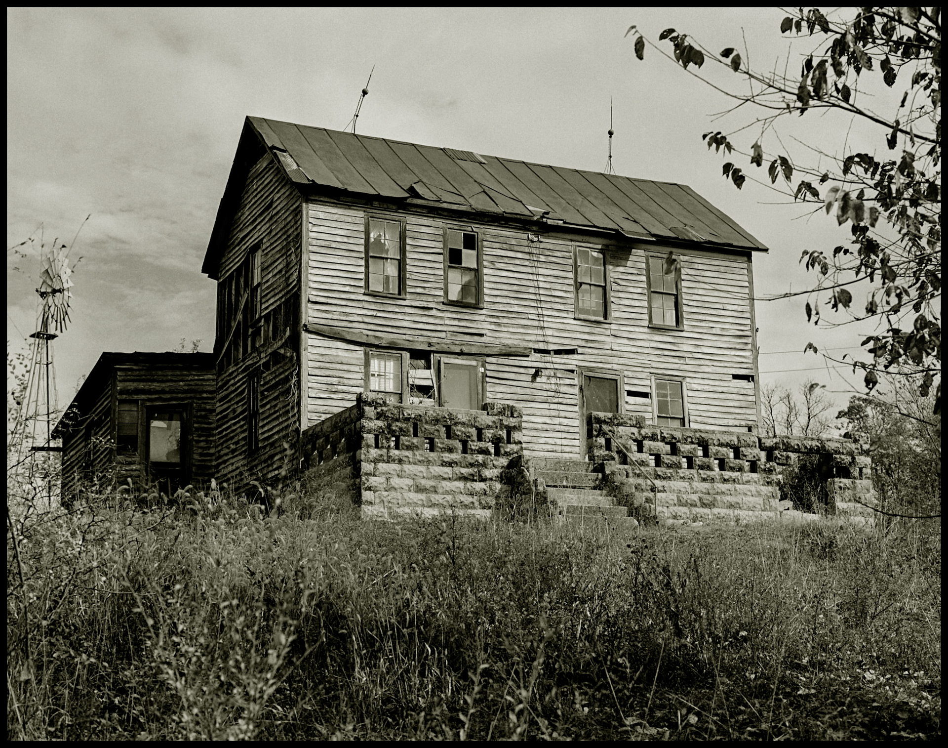 A sepia toned black and white vintage image of an abandoned house on a hilltop with a windmill out back in rural Northern Misouri. Yarrow, Missouri, USA, 1978.