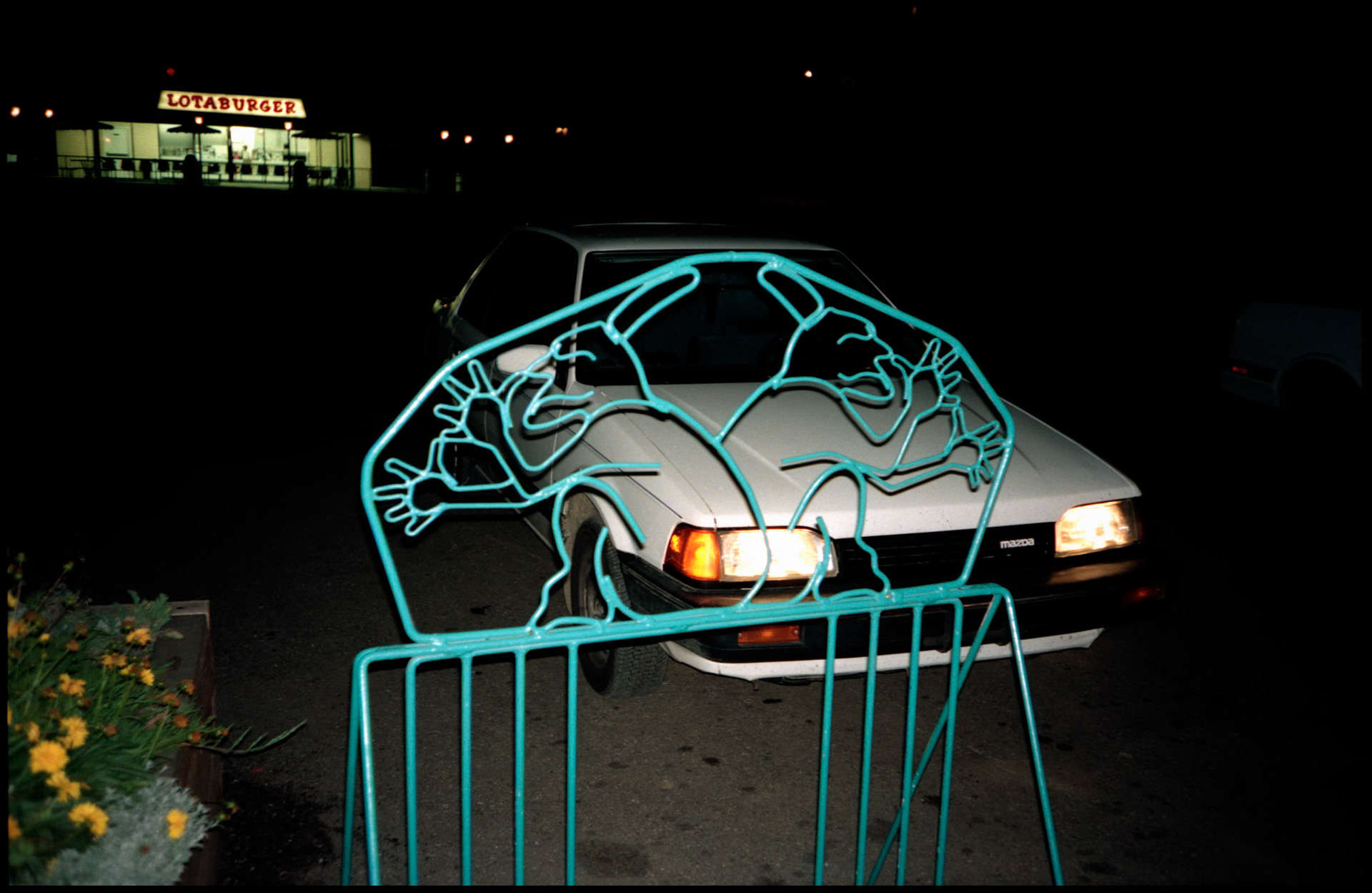 Interesting bicycle stand outside of a vegetarian restaurant in Taos New Mexico with gnomes, seemingly, thumbing their noses at the Lotaburger hamburger stand across the street. 1993