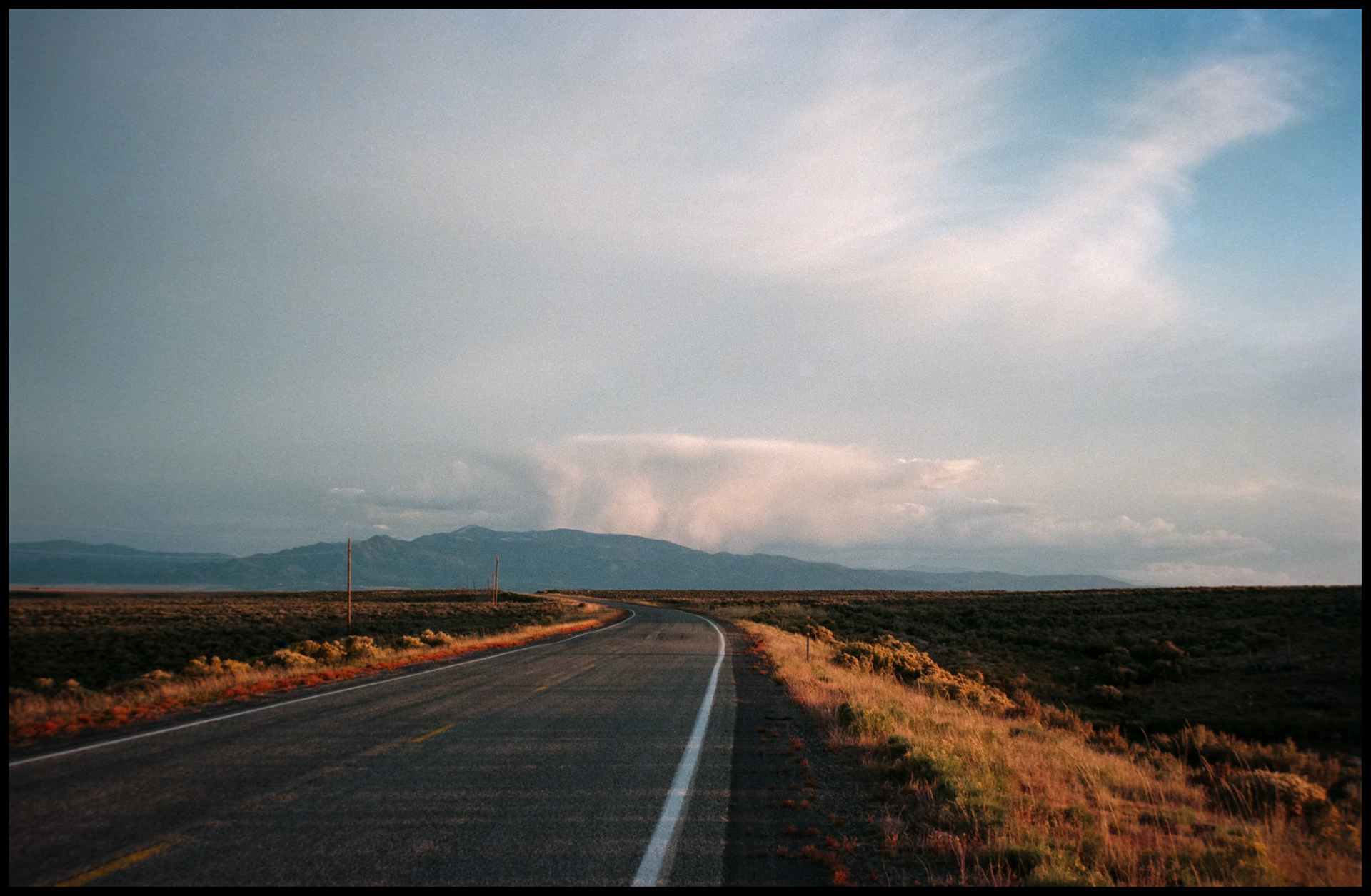 A lonely stretch of New Mexico highway leading toward a mountain with a storm raging above. 1993