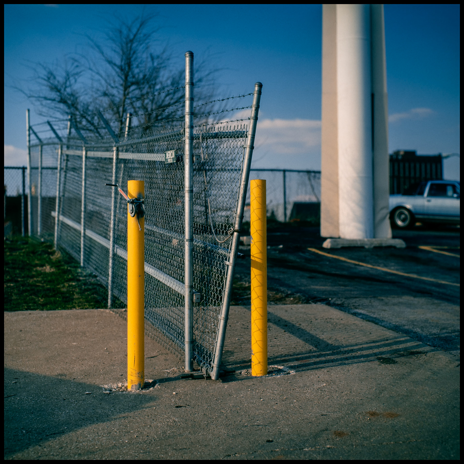 Two yellow parking bollards protecting a gate of a fence in a parking lot behind a Denny's restaurant in Kansas City in 1985.