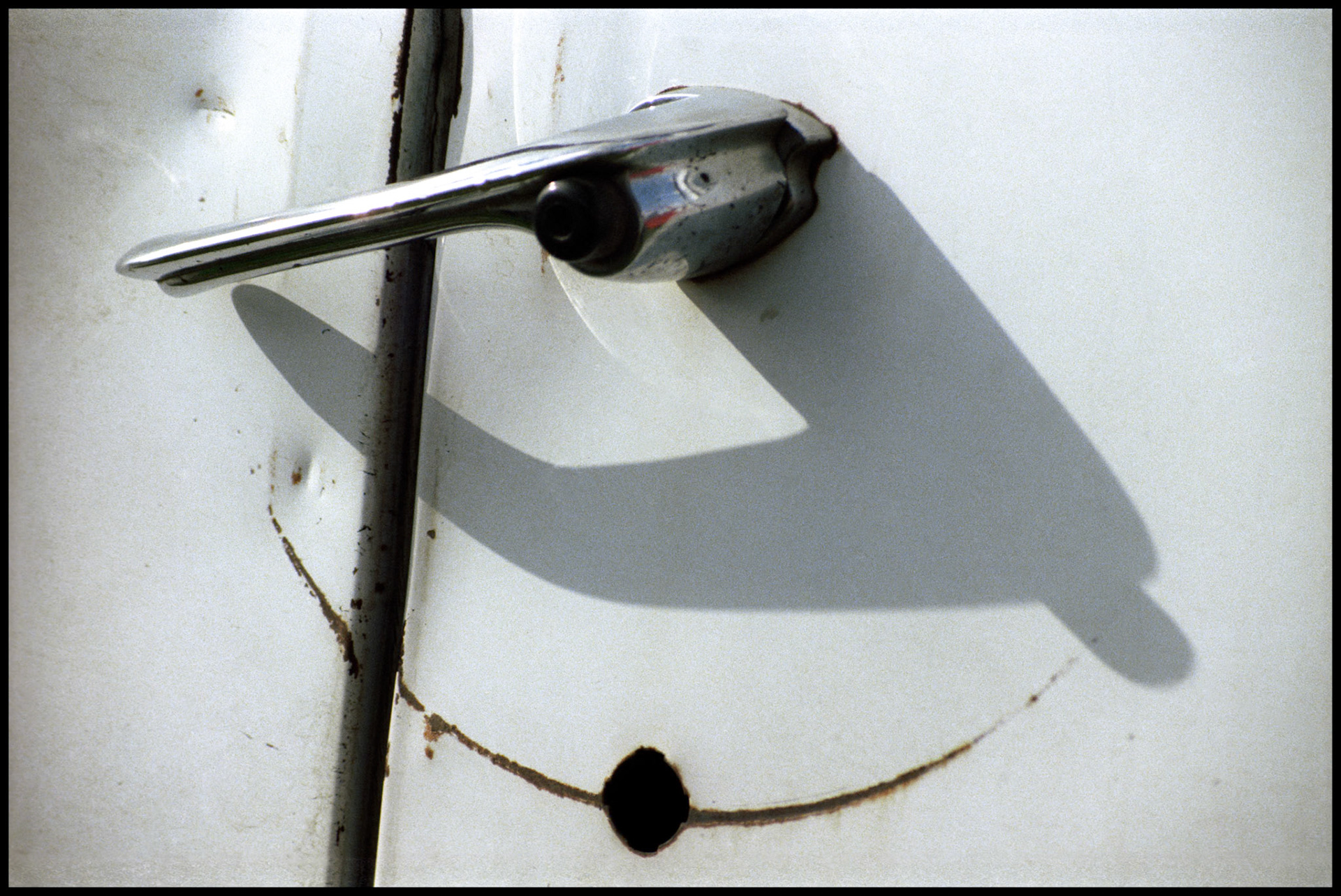 Detail of the handle on a 1966 Chevrolet van side door, casting a shadow on  the rest of the door that interacts with the arc of a scratch caused by the broken handle, making an interesting design. 1981