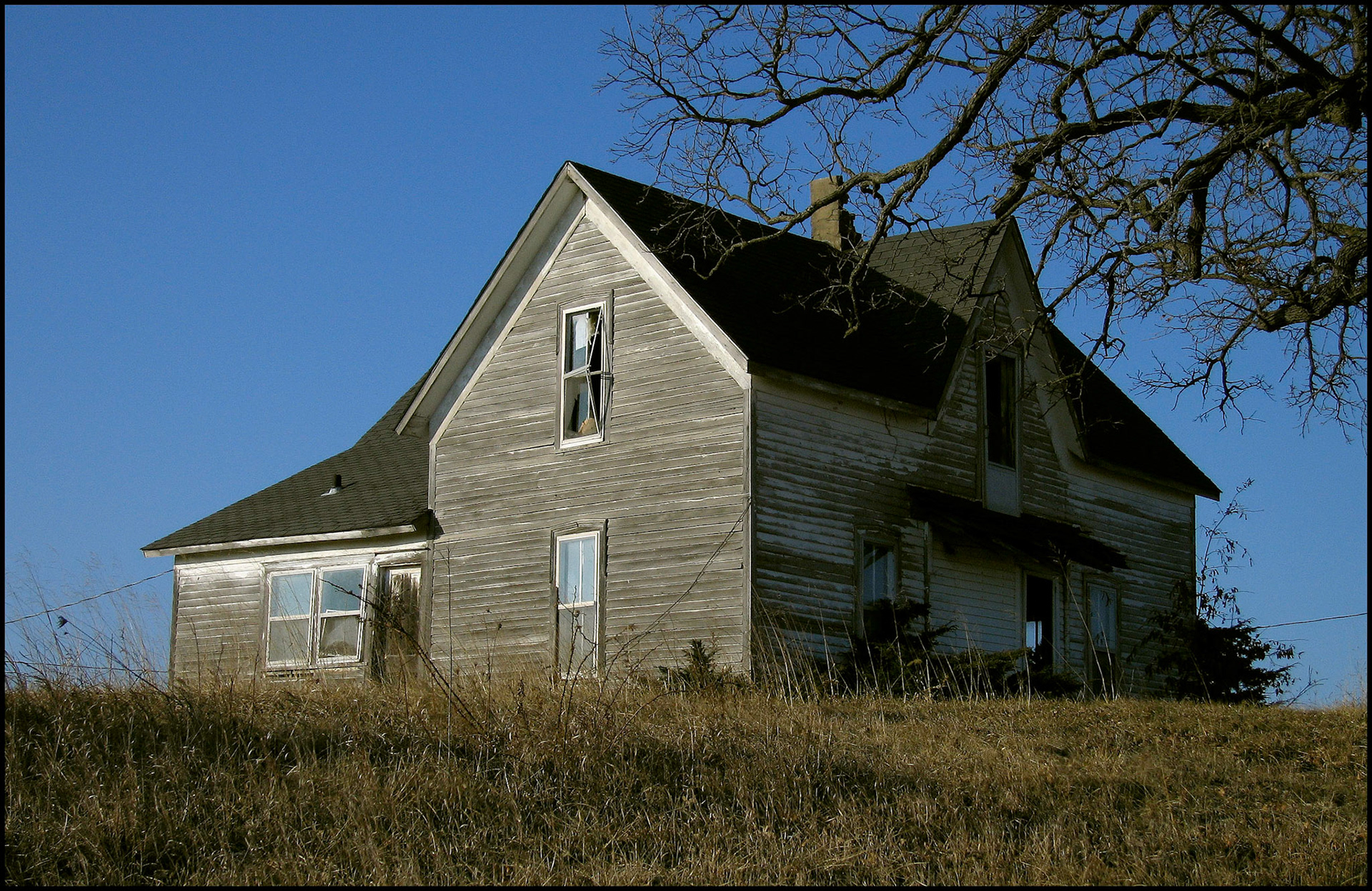An abandoned house on a hill, side lit by the early morning light with a broken window. Near Pure Air, Missouri USA 2007