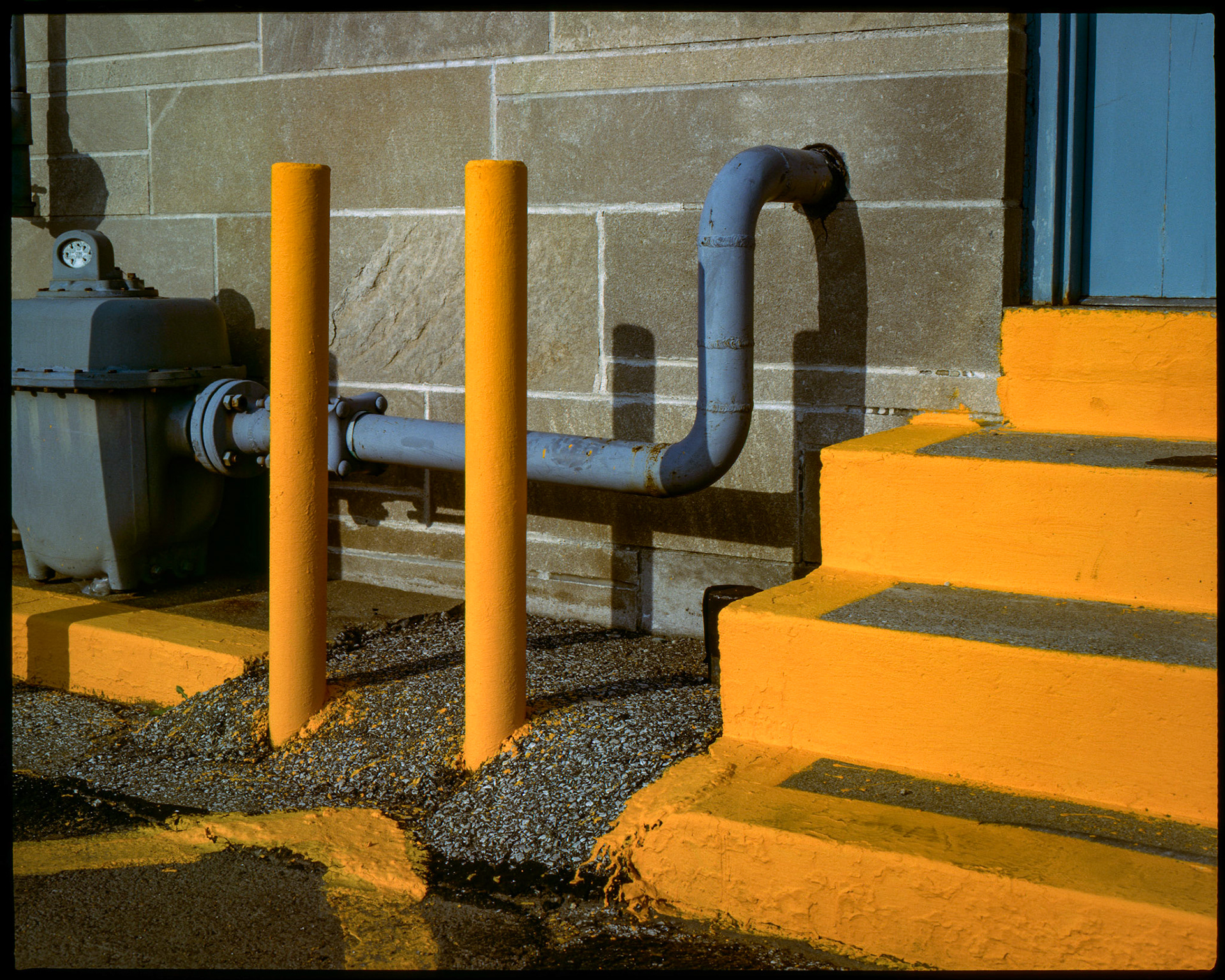 An minimal abstract geometric study of bright yellow steps, safety bollards, and a  gray gas meter at the rear door of a post office in Bloomington, Indiana in 1986. Part of my Industrial Geometry series.