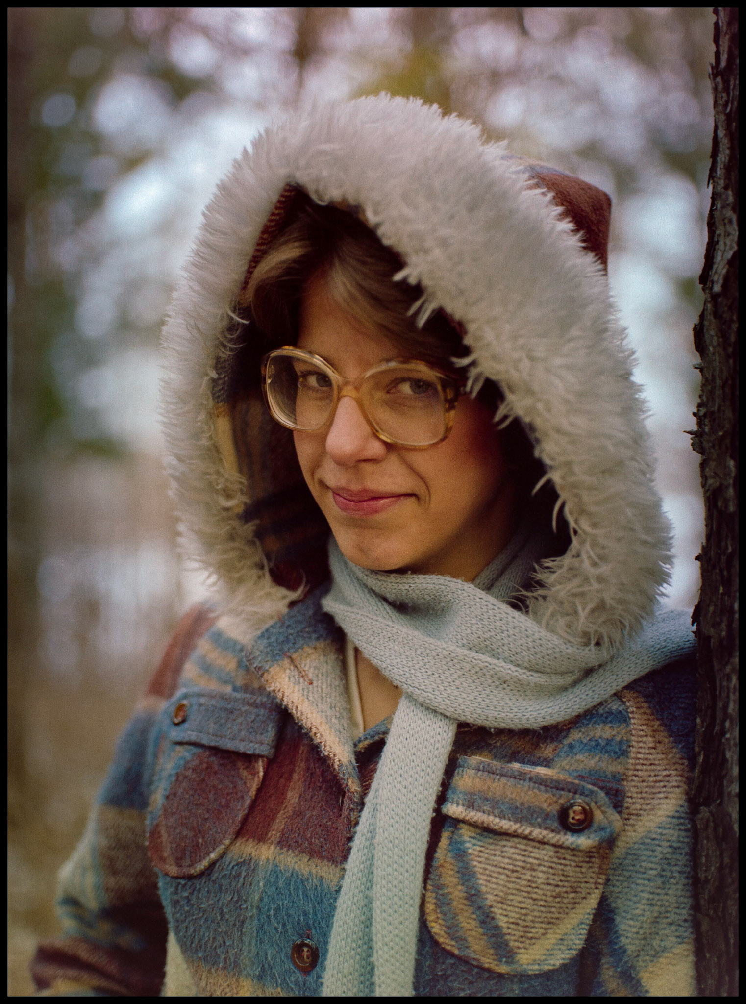 A woman in the woods wearing a hooded coat with a mischevious smile. Kirksville, Missouri 1980