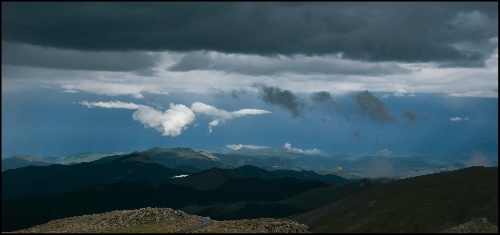 Colorado Rocky Mountain scenic of low hanging clouds against a dark sky above a highlighted mountain top and lake as viewed from Mount Evans Highway, Colorado USA, the highest paved road in the country.