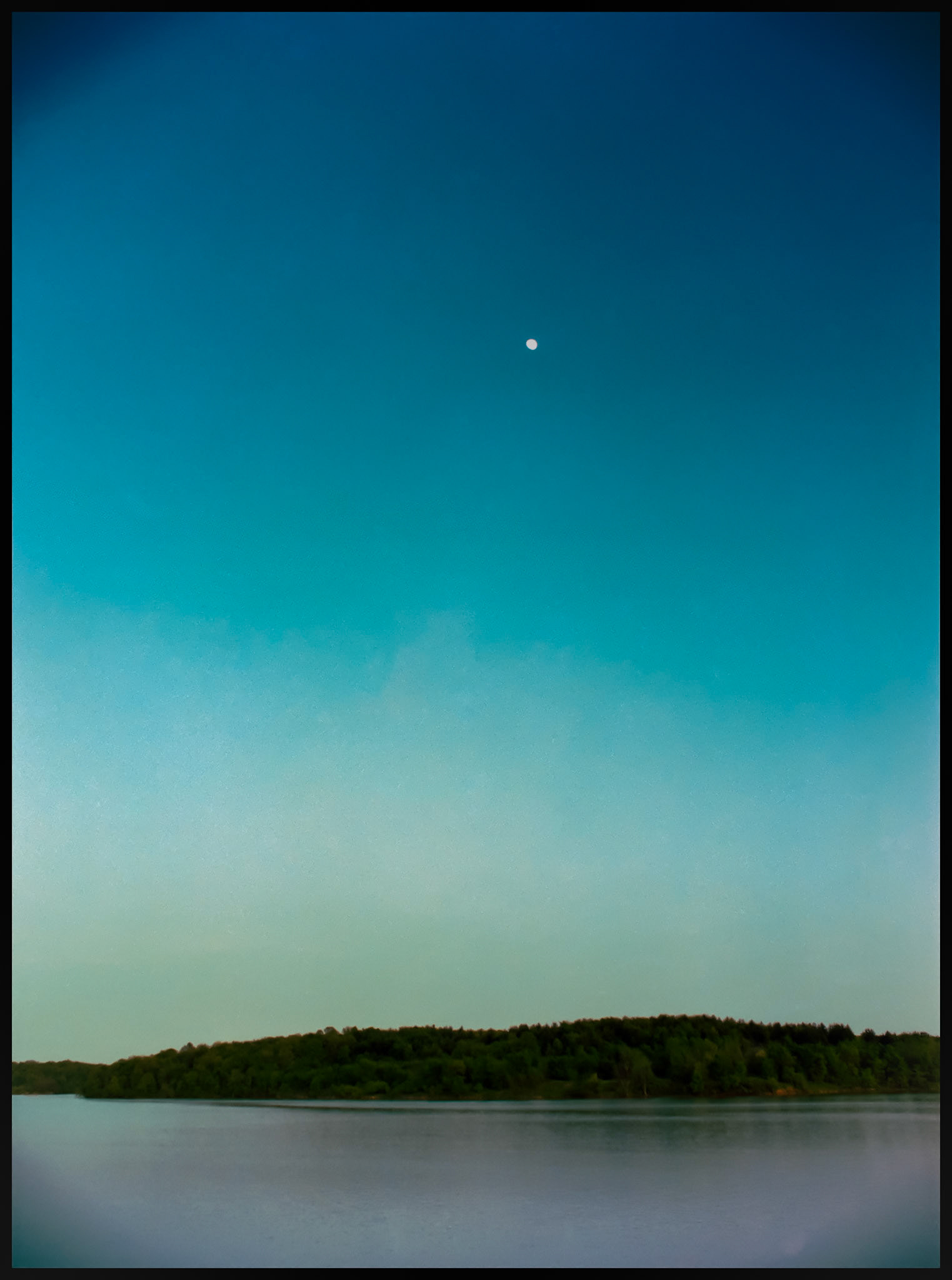 A nearly full moon in a deep blue dusk sky over a lake. Forest Lake at Thousand Hills State Park, Kirksville, Missouri 1983