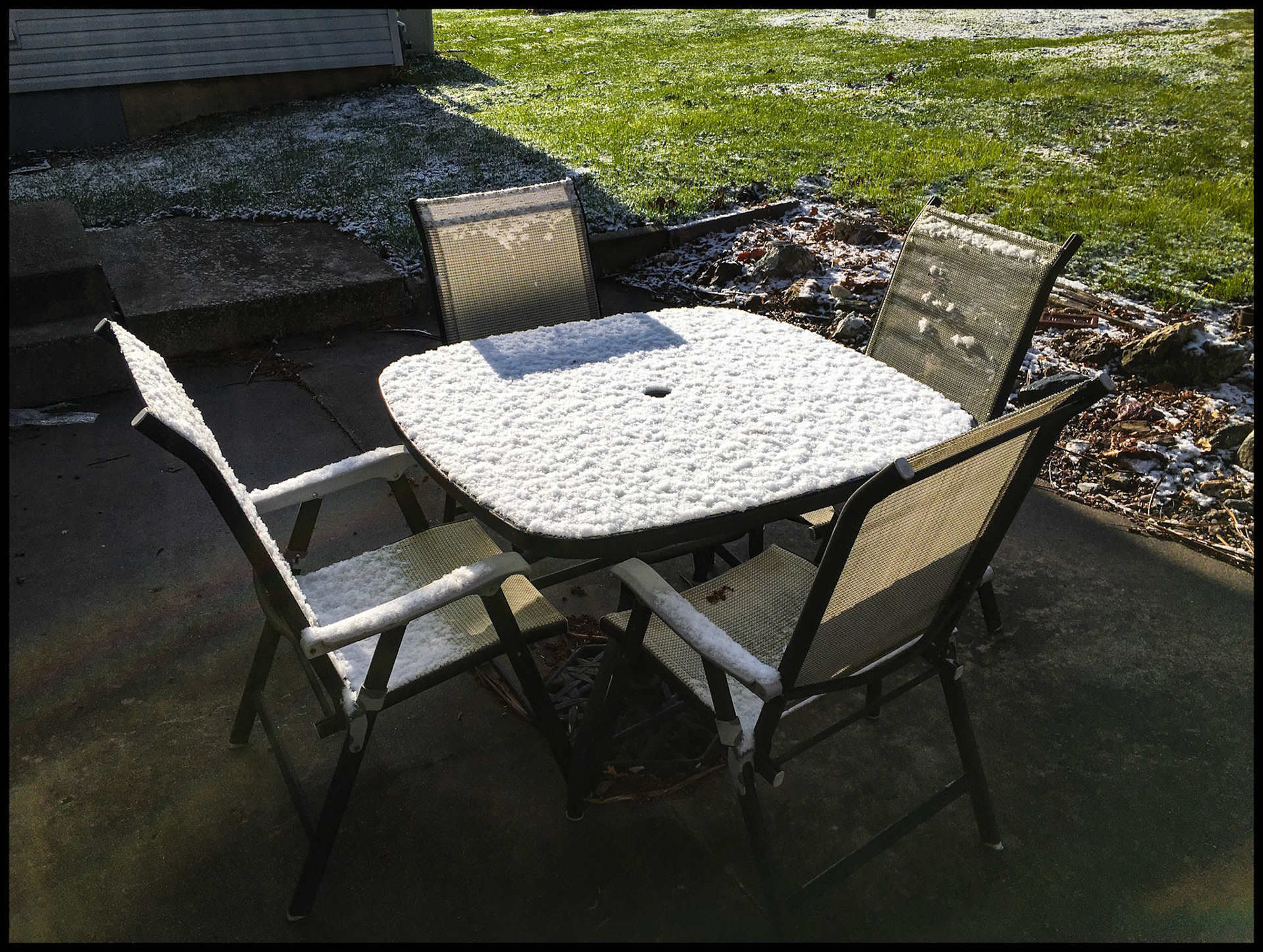 An abstract minimal composition of springtime snow on the patio table of a small town home highlighted by the early morning sun.  Kirksville, Missouri 2020