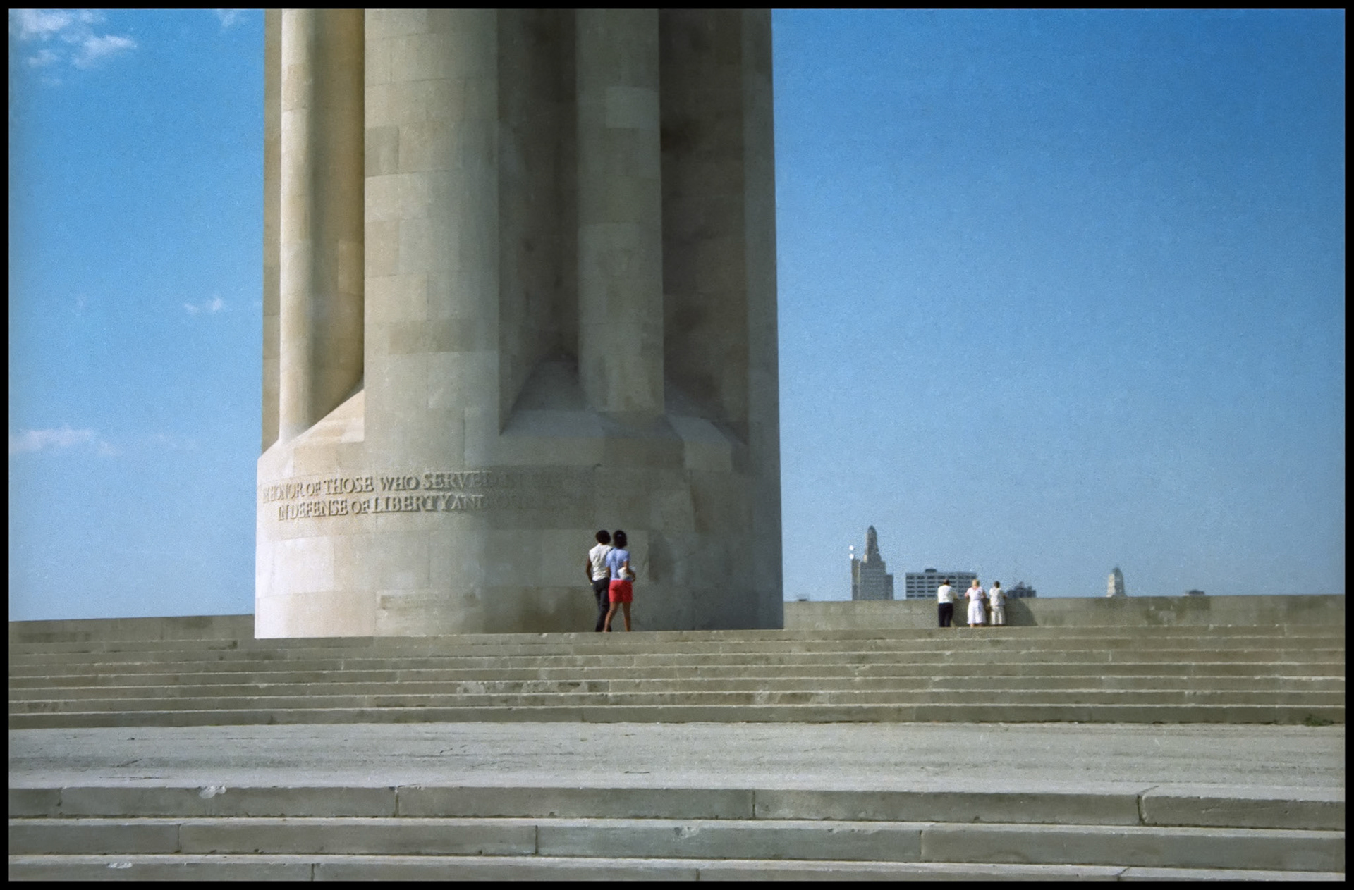 A vintage detail image of the base of the Liberty Memorial Tower and steps at Liberty Memorial Park showing strolling by and viewing the Kansas City skyline in the background. This was renamed as The National World War 1 Museum and Memorial in 2004, Kansas City, Missouri 1983.