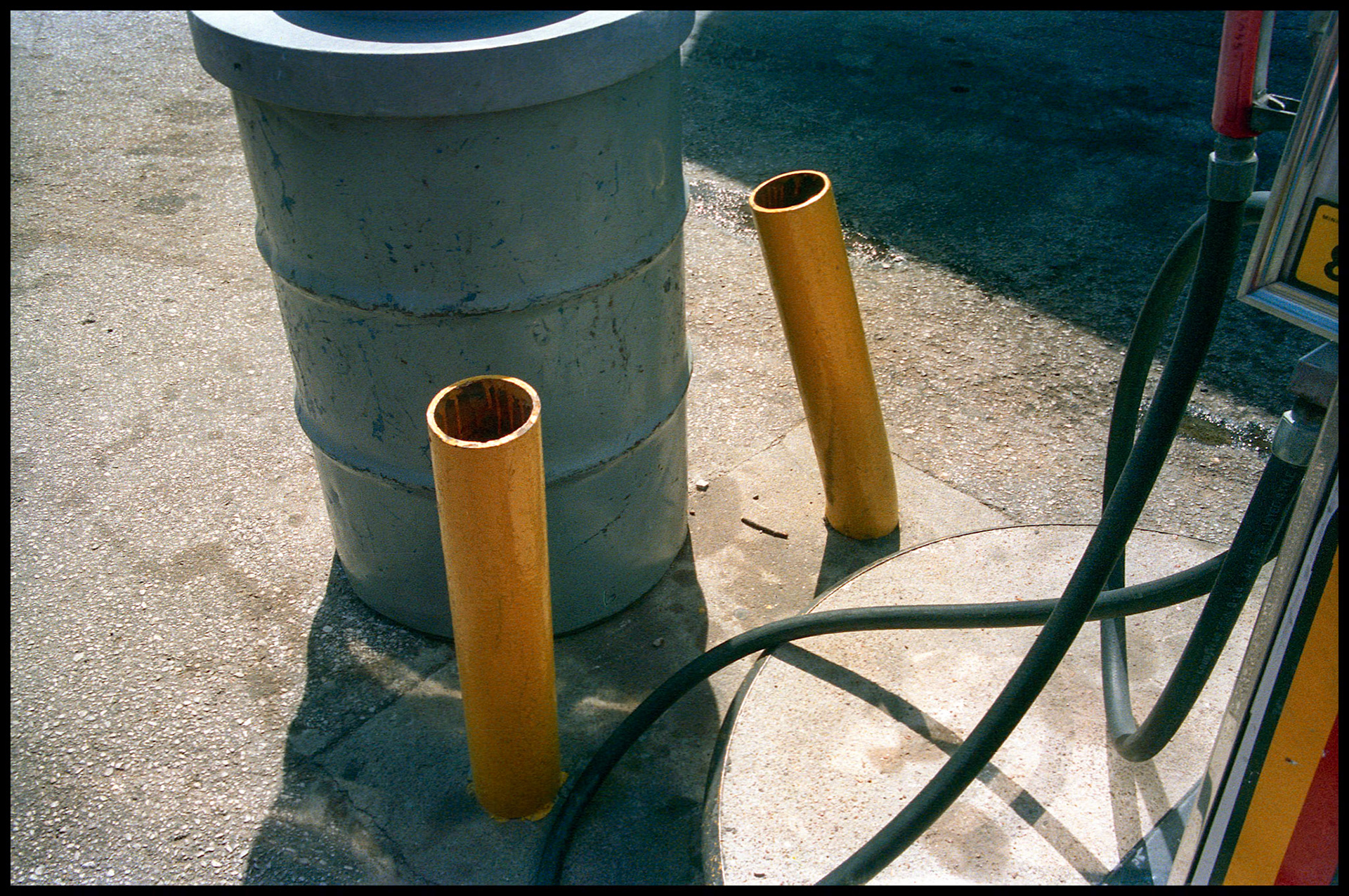 A gas pump hose, yellow poles, and trash can making interesting lines, shapes, and shadows. Columbia, Missouri 1986