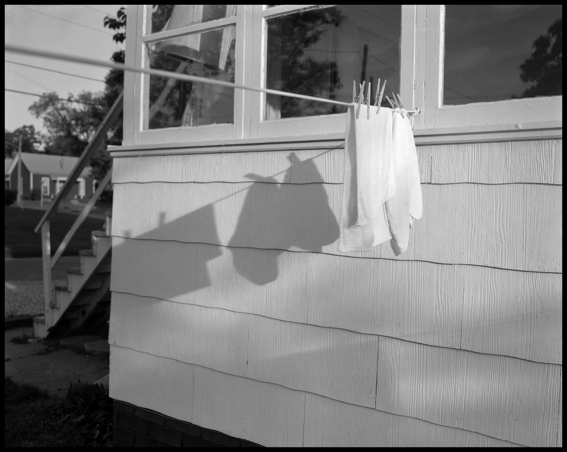 A minimal view of the shadow cast by laundry on a backyard clothesline onto the back porch of a house by the evening sun. Kirksville, Missouri 1984