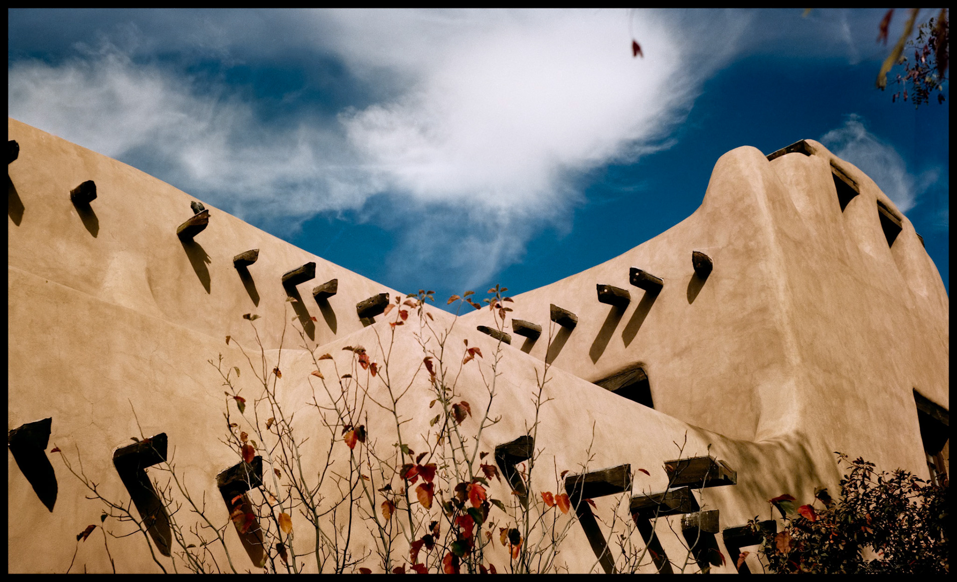 A detail view of a wall of the adobe building St. Francis Auditorium in Santa Fe, New Mexico 1993 which highlights it's interesting lines and overall design with a very interesting cloud filling the sky background.