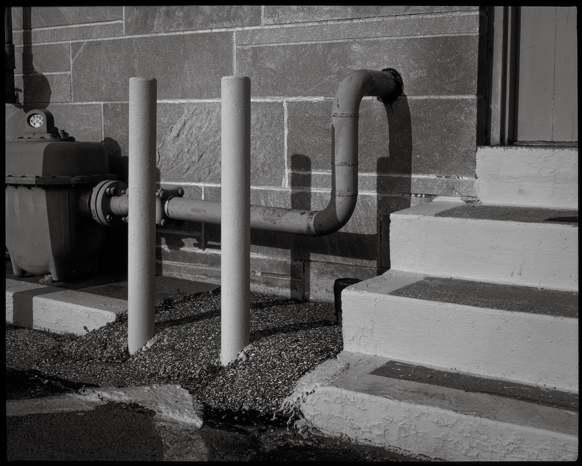 An minimal abstract geometric study of bright yellow steps, safety bollards, and a  gray gas meter at the rear door of a post office in Bllomington, Indiana in 1986. This is part of my Industrial Geometry series.
