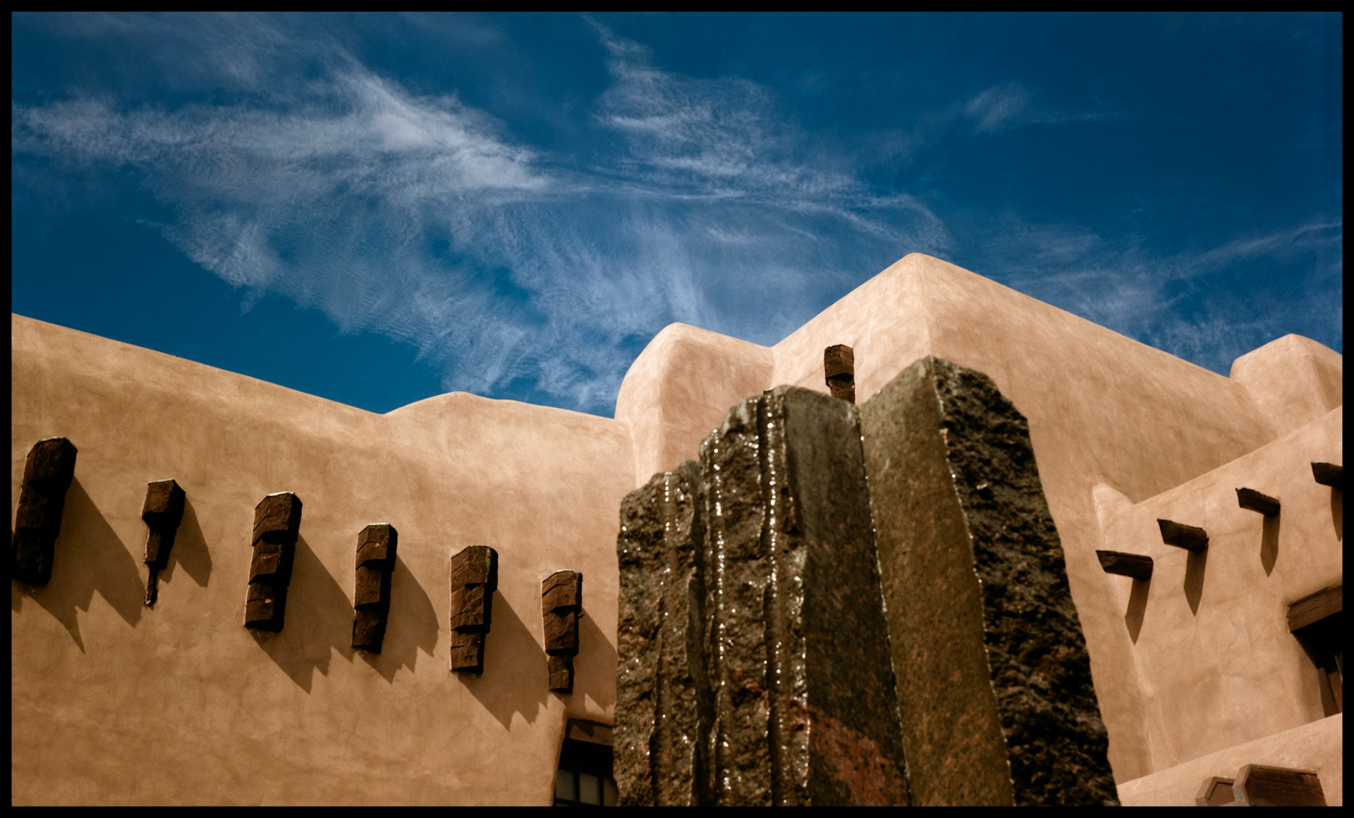 An interesting juxtaposition between the walls of the inner courtyard of the New Mexico Museum of Art and its fountain sculpture blurred in the foreground and the whispy Cirrus clouds adorning the deep blue sky in the background. Santa Fe New Mexico USA 1993