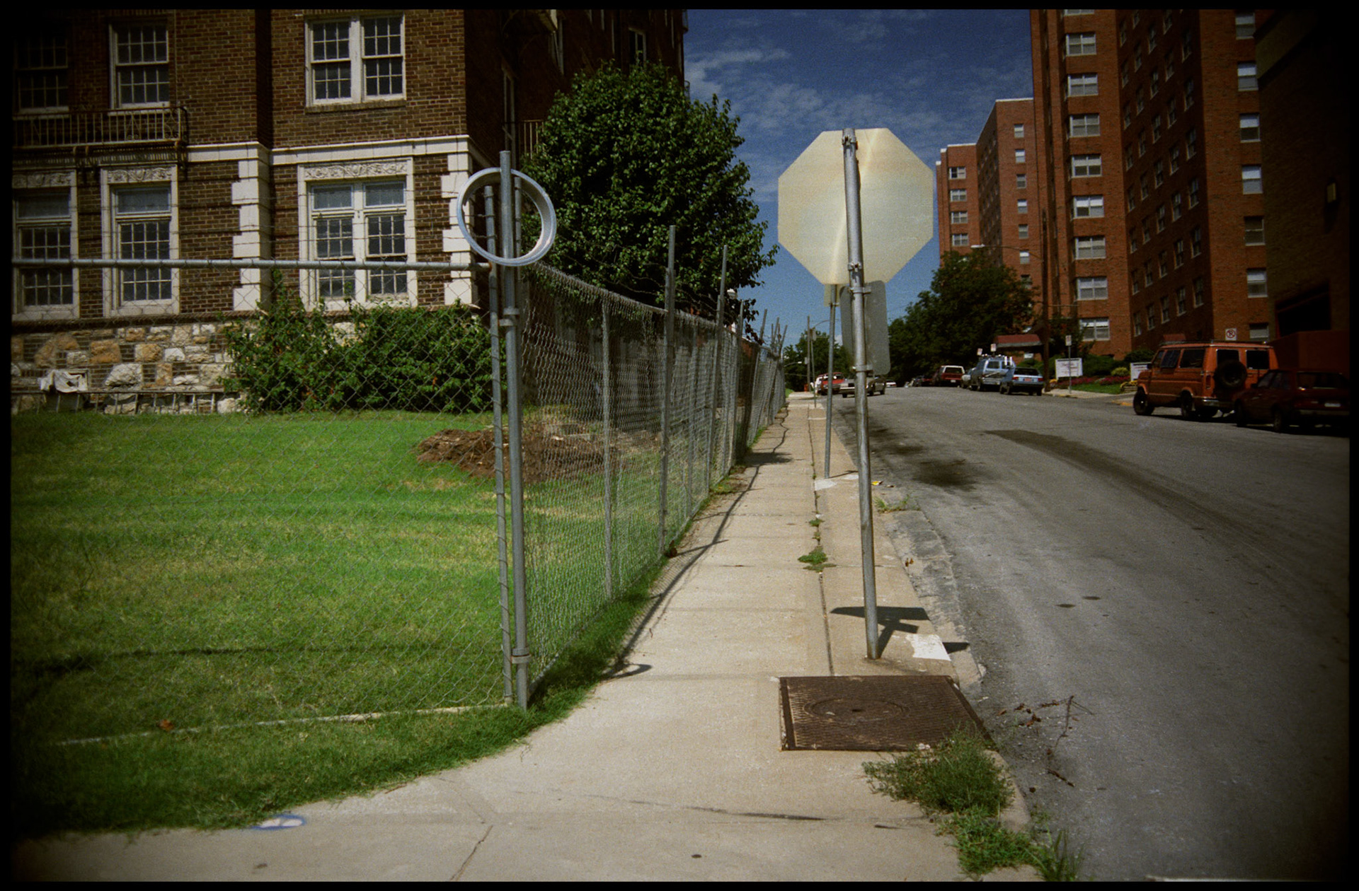 Urbanscape of sidewalk, street,stop sign, and chain link fence. Kansas City, Missouri, 1990