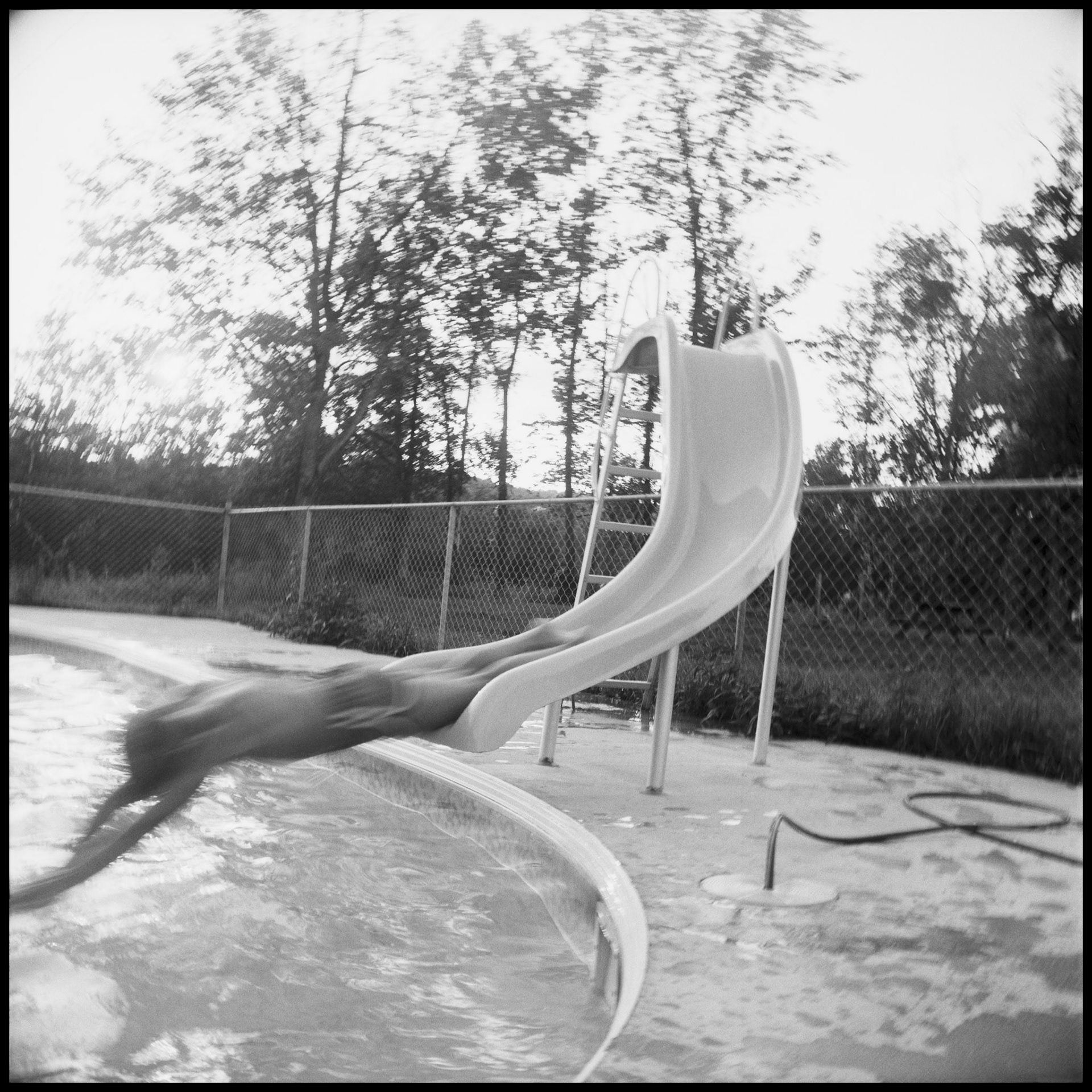 A motion blurred vintage image of an adolescent boy coming off off a slide head first into a swimming pool. Near Marshall, Missouri 1977