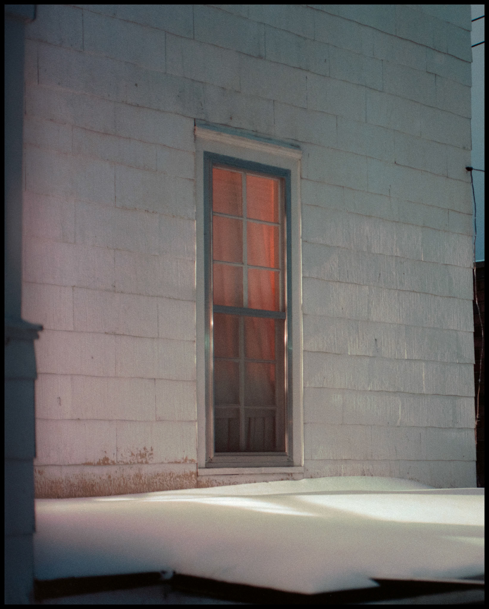 Warm colored light passing through the curtain of a house window and light from a porch on the exterior shot on a cold snowy night. Kirksville, Missouri 1984